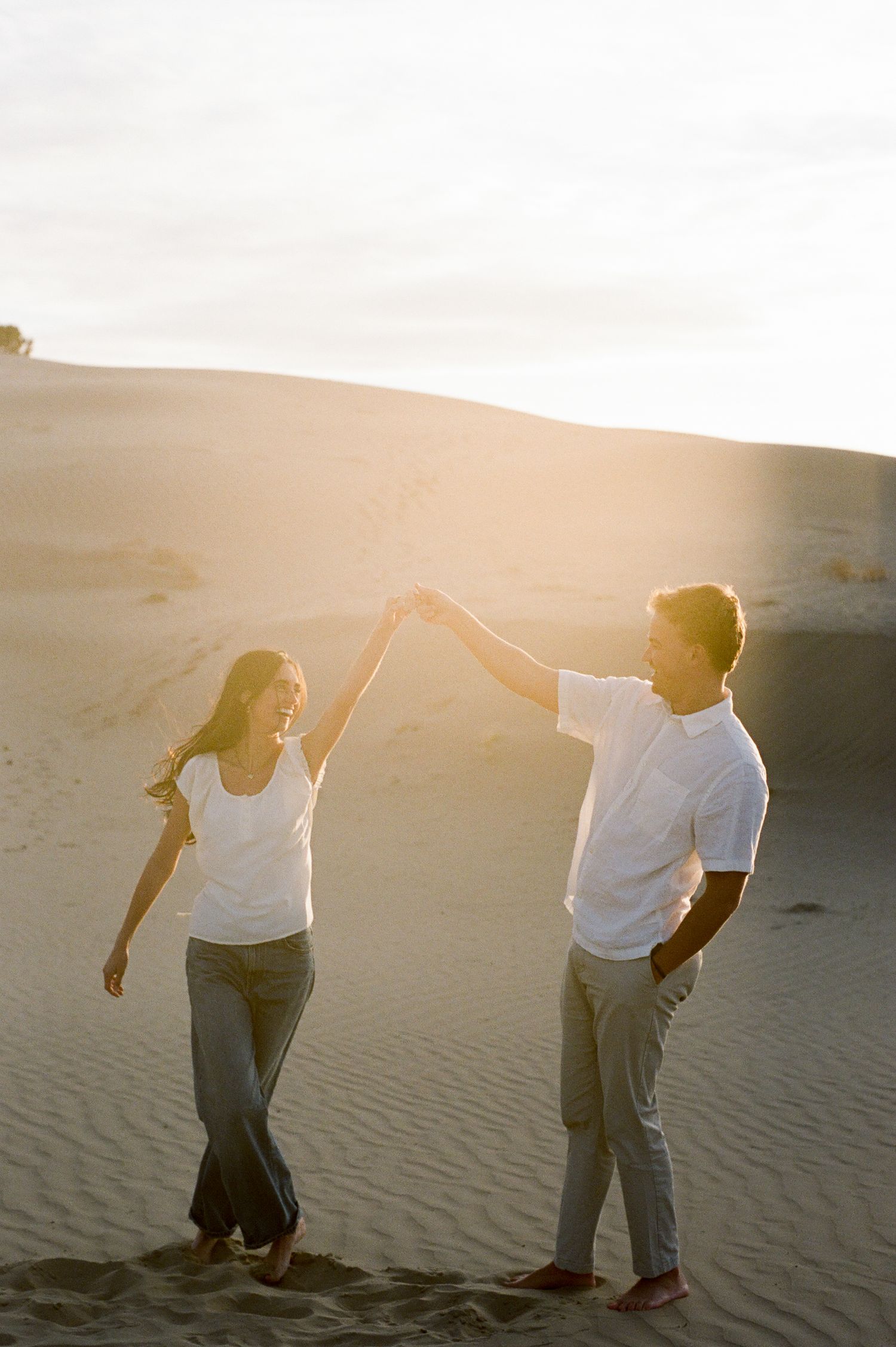 Couple dancing and holding hands on sand dunes during golden hour sunset at Little Sahara Sand Dunes.