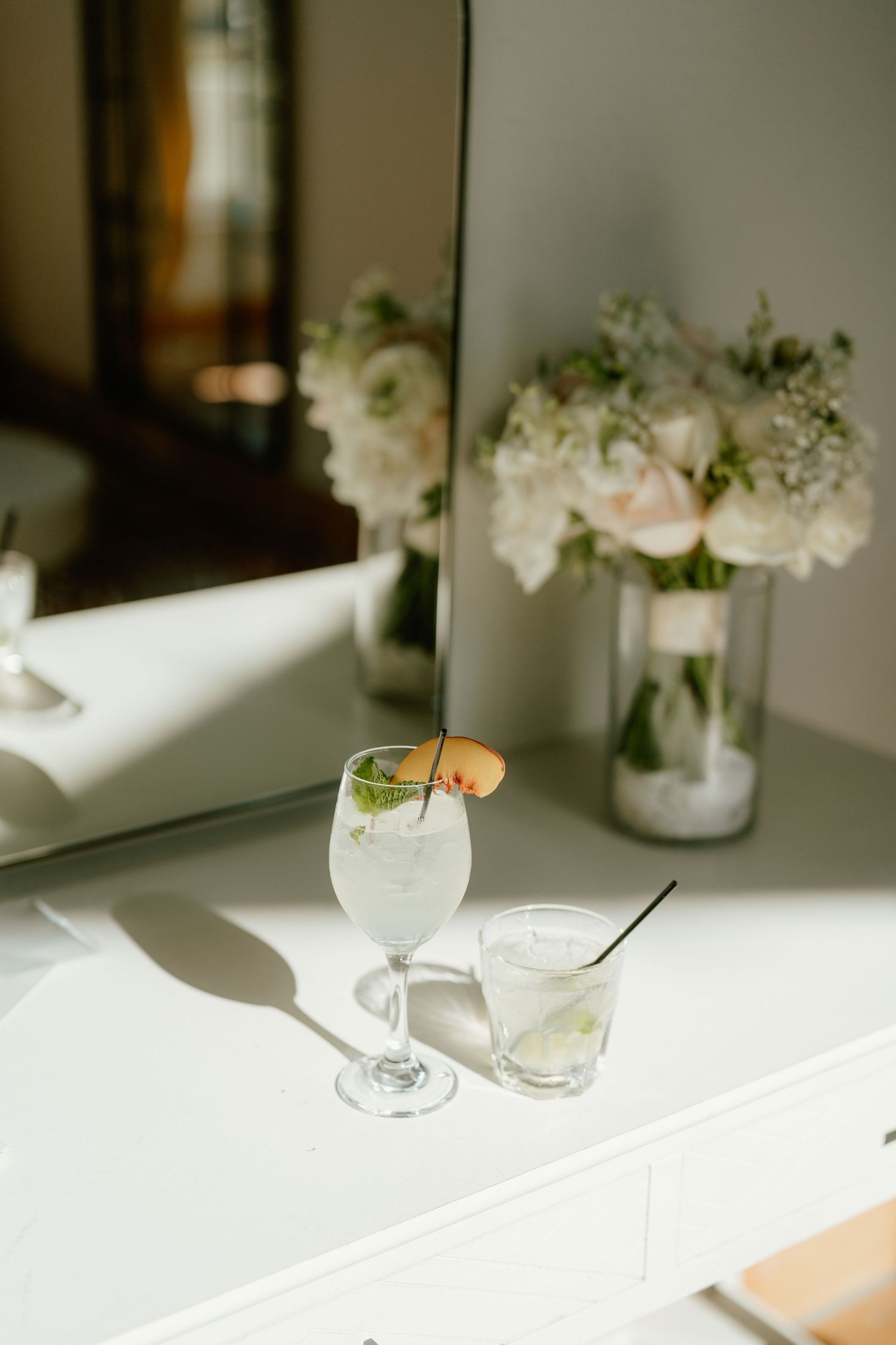 Elegant cocktails on white vanity with floral bouquet and mirror, perfect for a wedding reception setting.