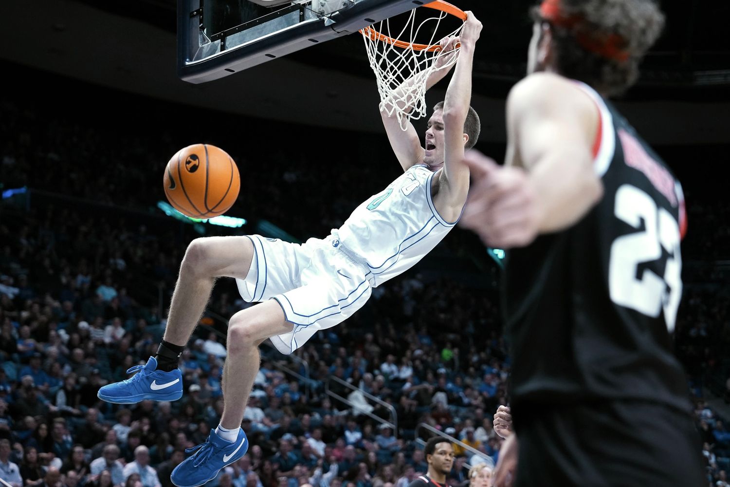 Basketball player dunks the ball during an intense college game while an opponent watches nearby.