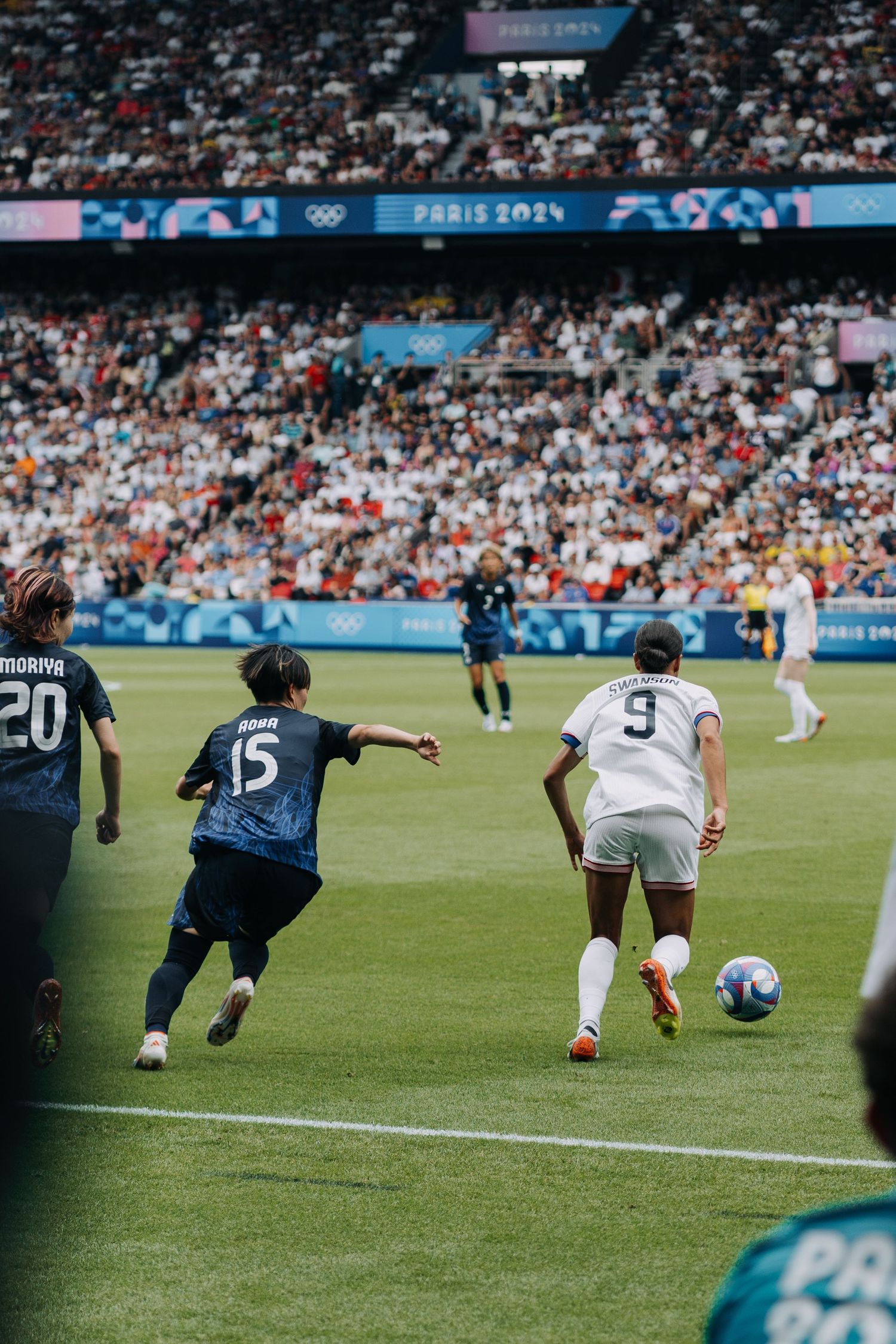Female soccer players chase the ball during an intense match at the Paris 2024 Olympics.