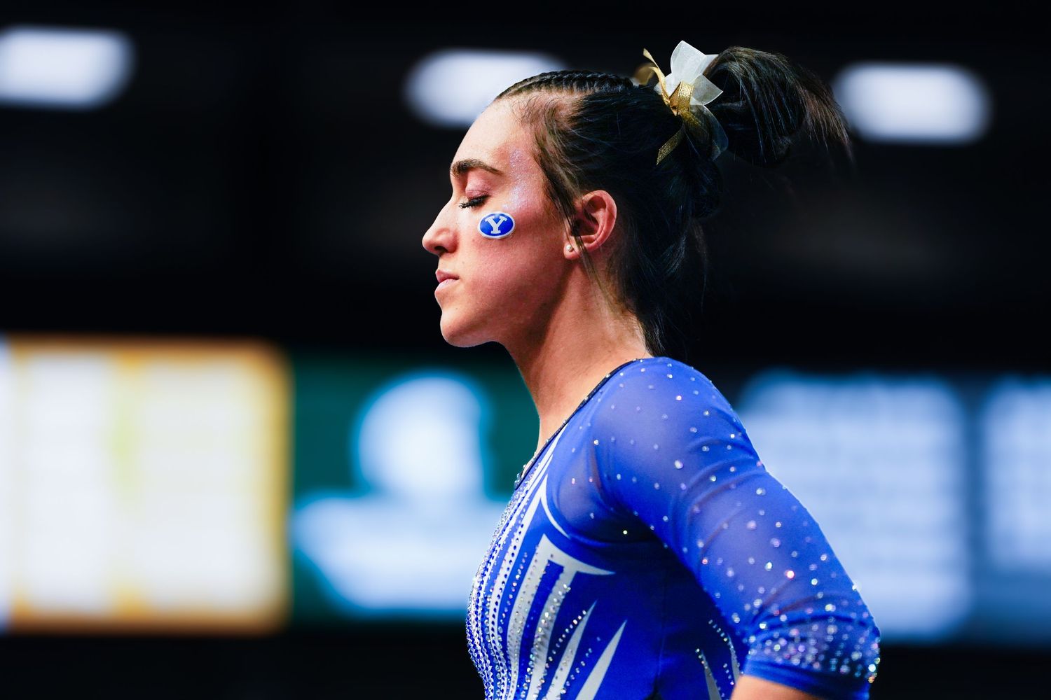 A focused female gymnast in a blue leotard with face paint prepares for her routine at a competition.