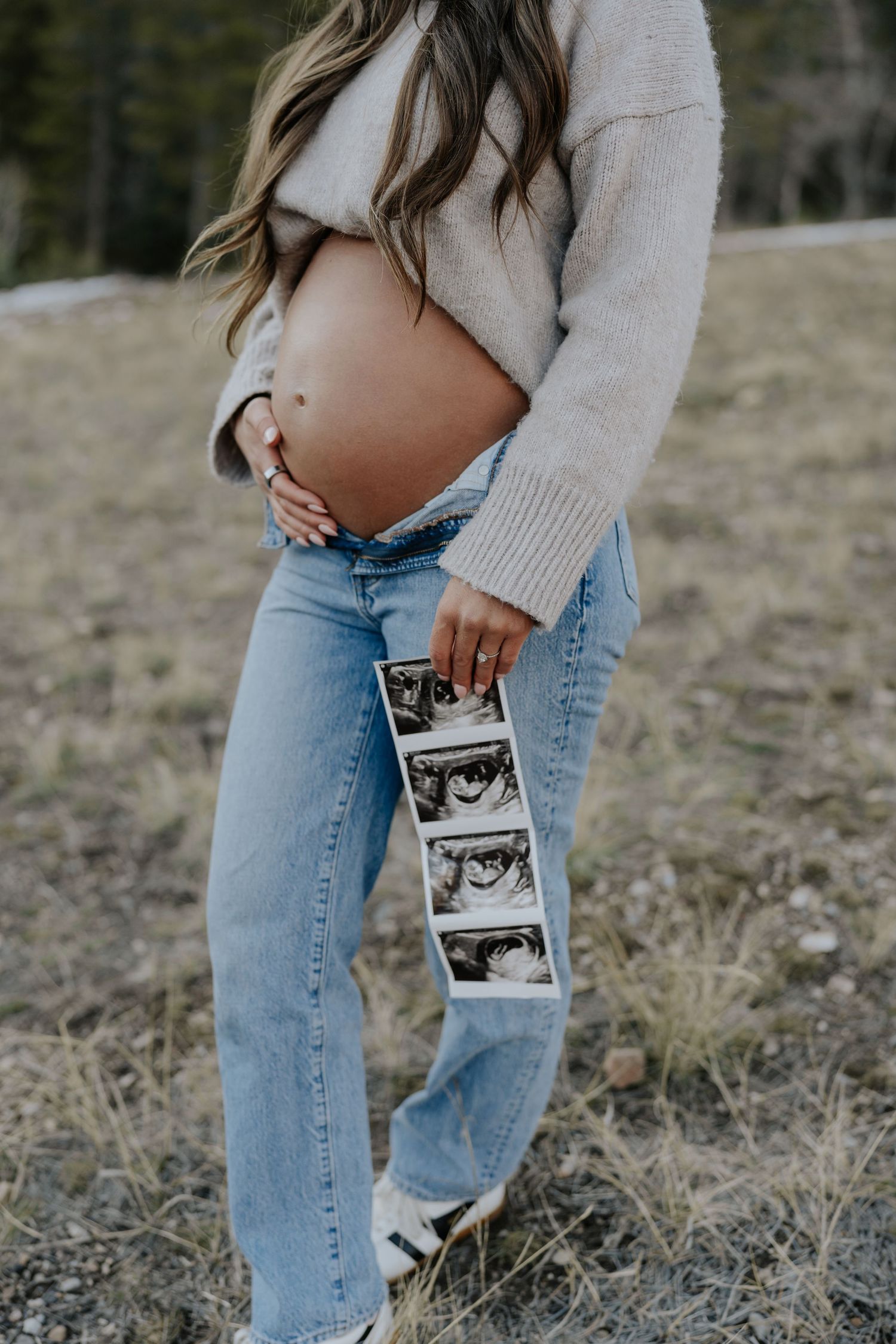 Close-up of pregnant woman holding ultrasound strip beside bare baby bump outdoors.
