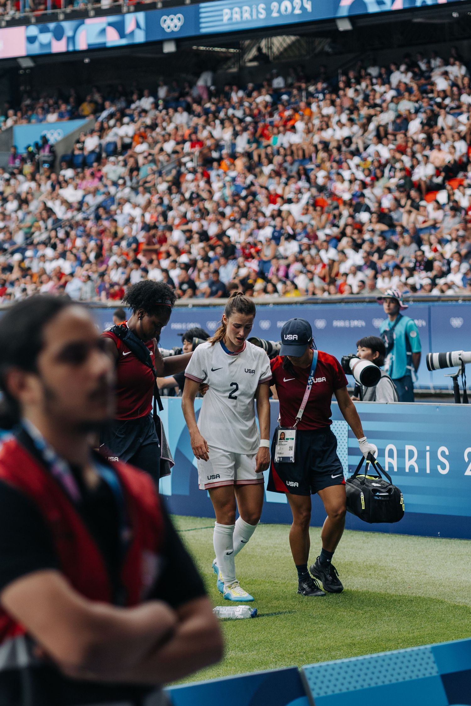 Injured female soccer player number 2 is escorted off the field at Paris 2024 Olympics.