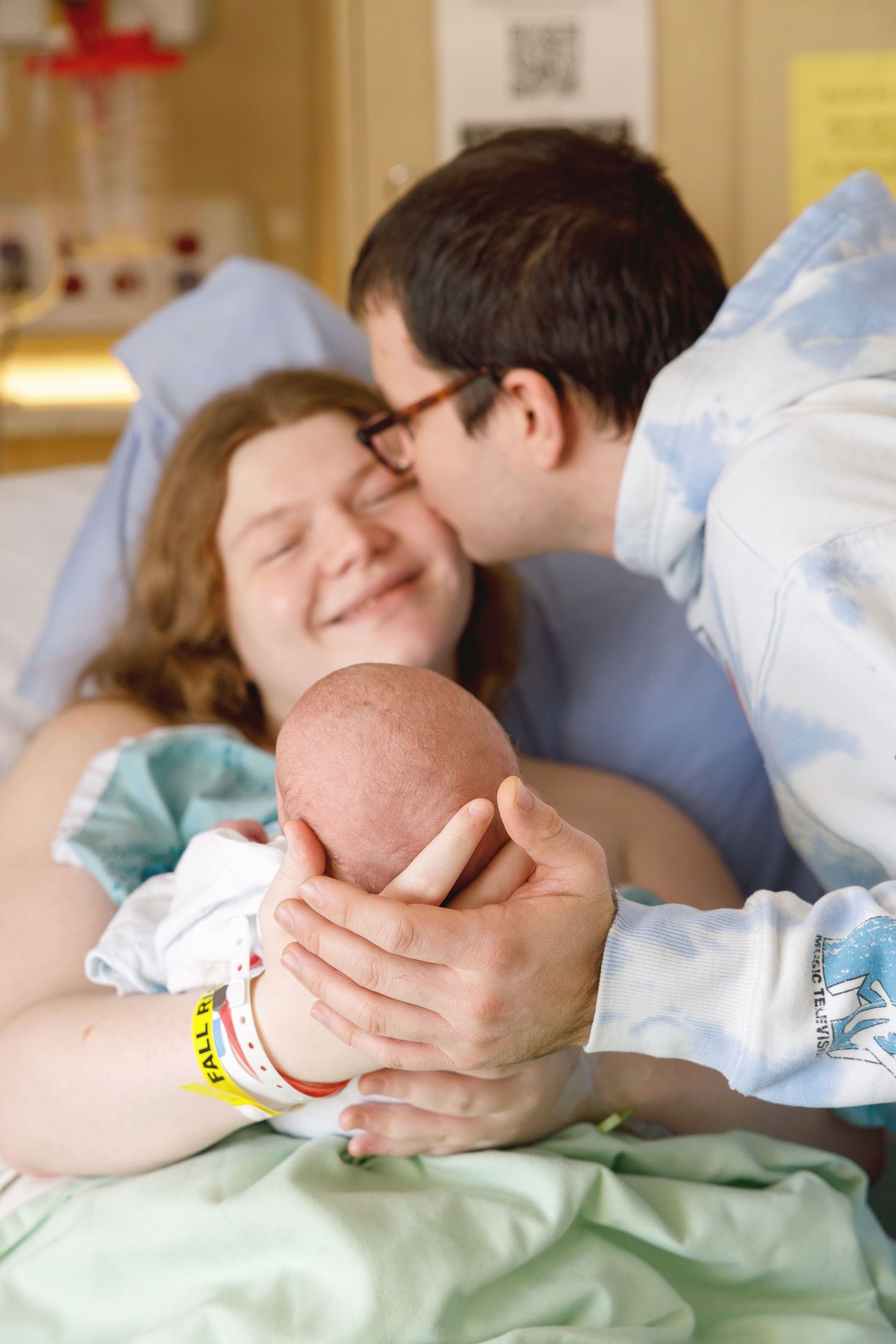 A tender moment in a hospital room as new parents cradle their newborn baby together in a joyful embrace.