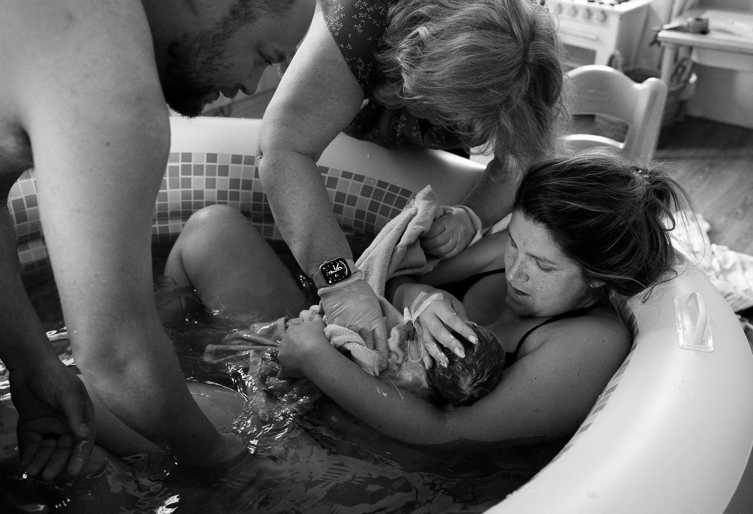 Black and white photograph showing a water birth in progress with supportive birth team members attending in a bathtub.