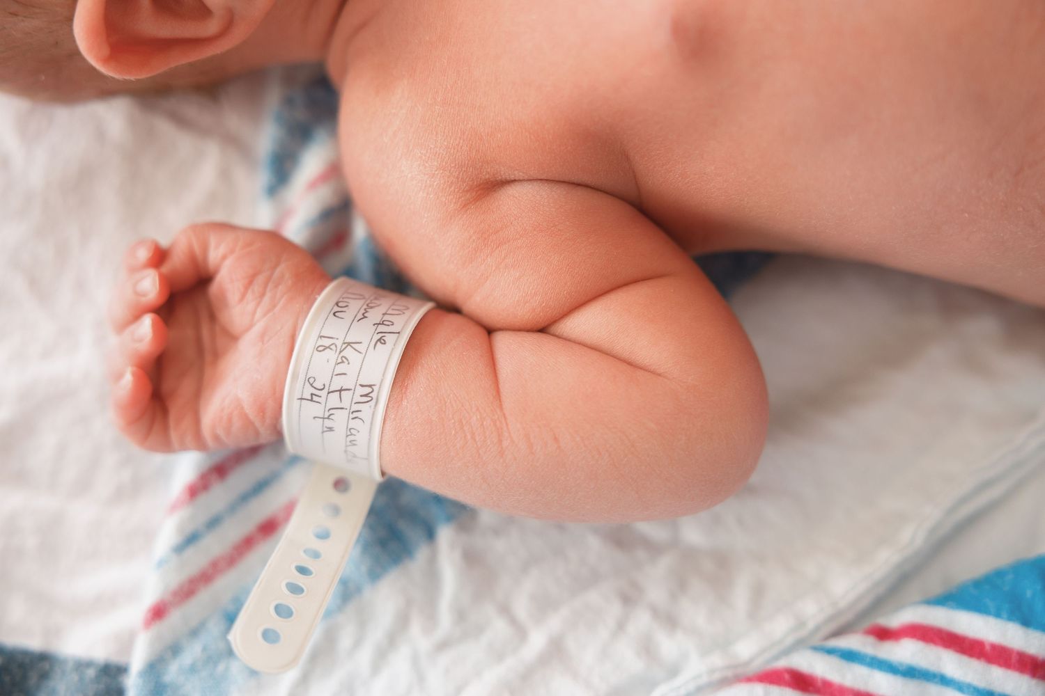 Close-up of newborn baby's arm with hospital identification bracelet against striped blanket.