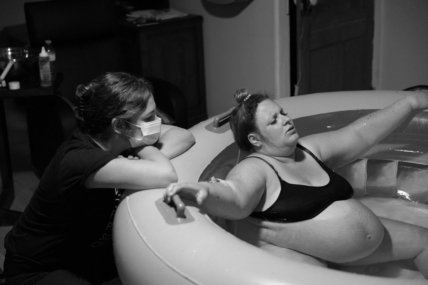 A black and white image shows a person receiving massage therapy on a treatment table in a dimly lit room.