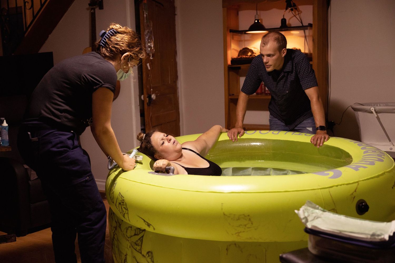 A person relaxes in a bright green birthing pool while receiving support during labor at home.