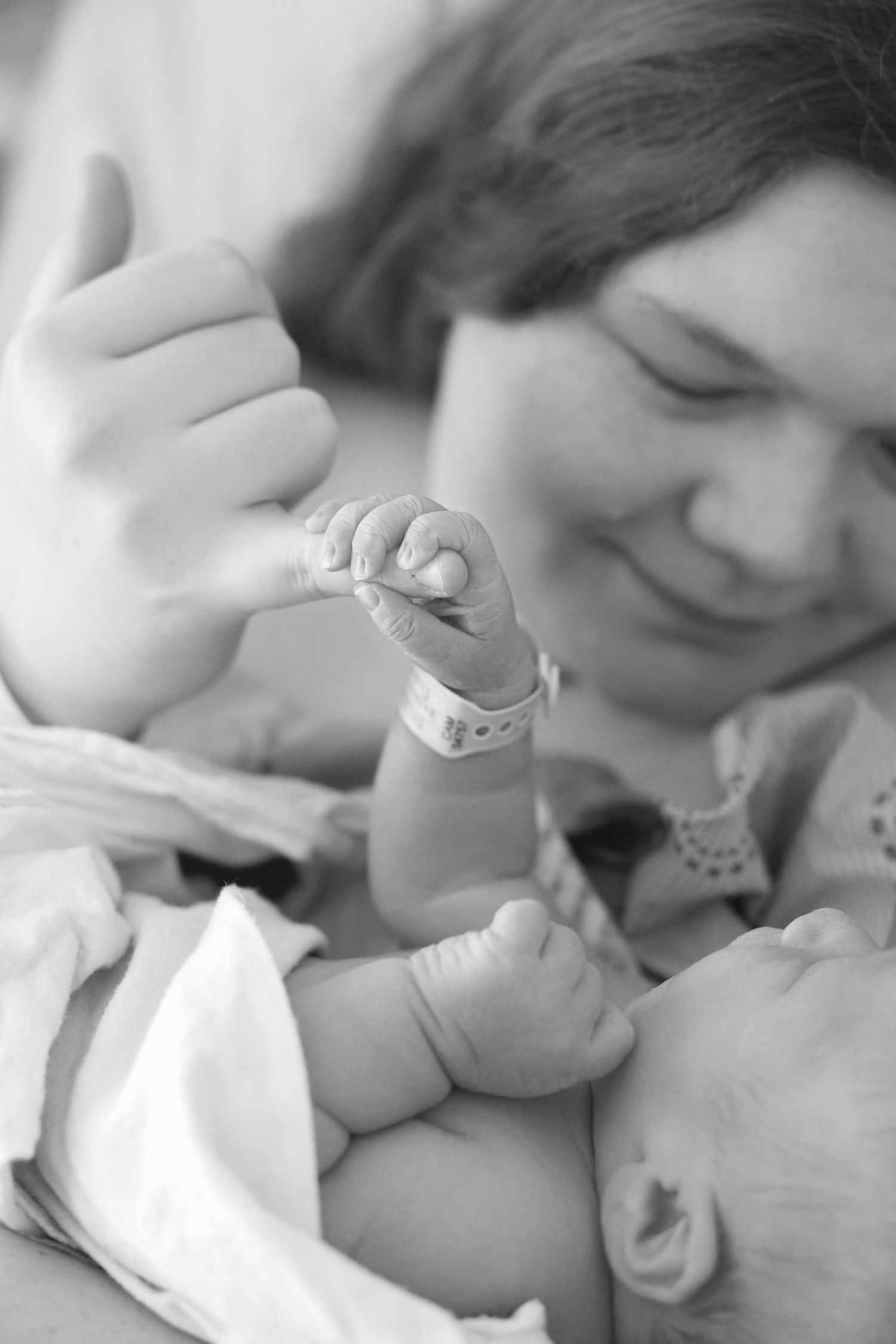 A tender black and white image shows a parent holding and admiring their newborn baby's tiny hand.