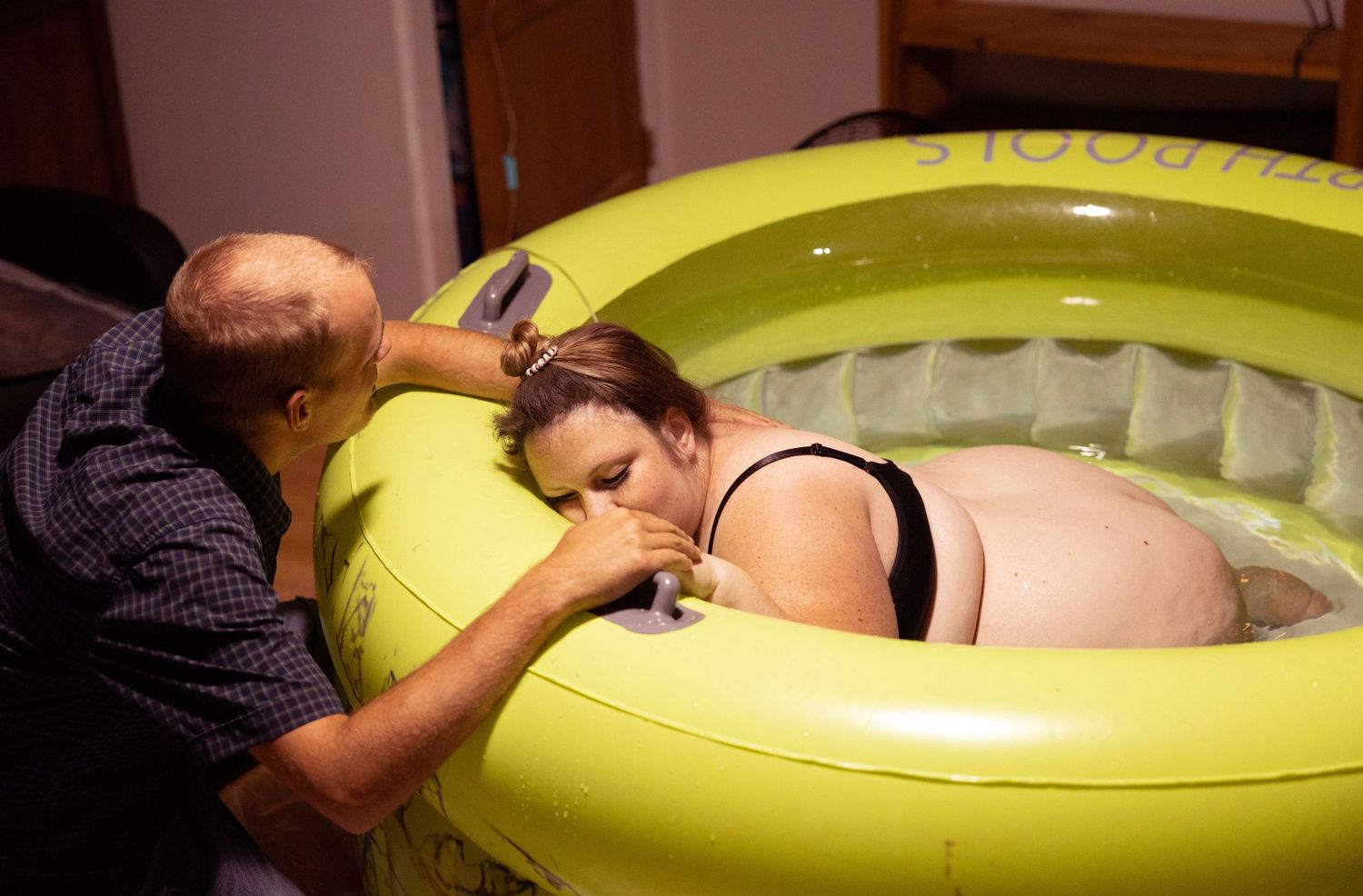 Two people sit next to a bright yellow inflatable birthing pool during labor preparation.