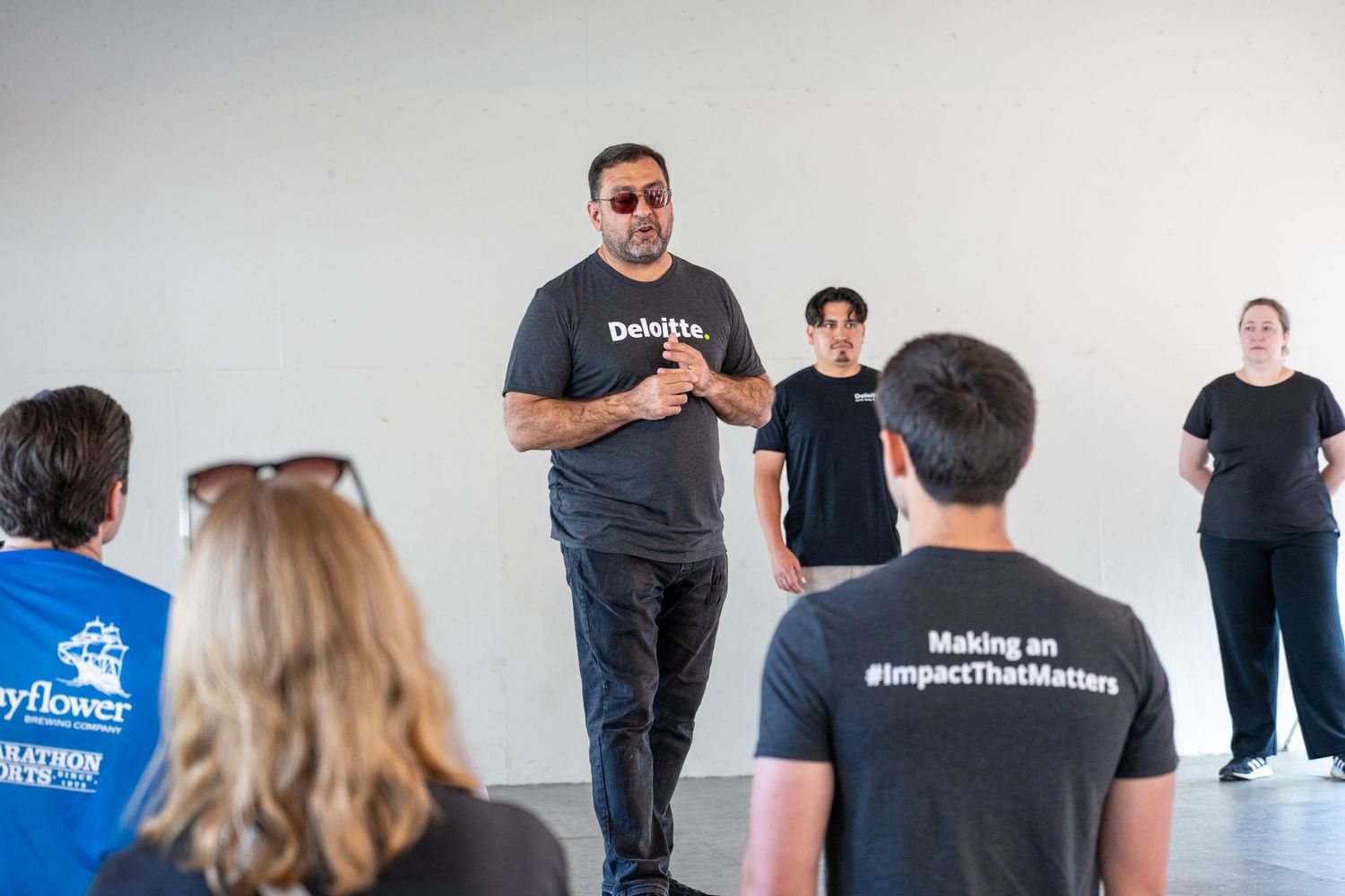 A group of people in black t-shirts attend a workshop session in a bright room.
