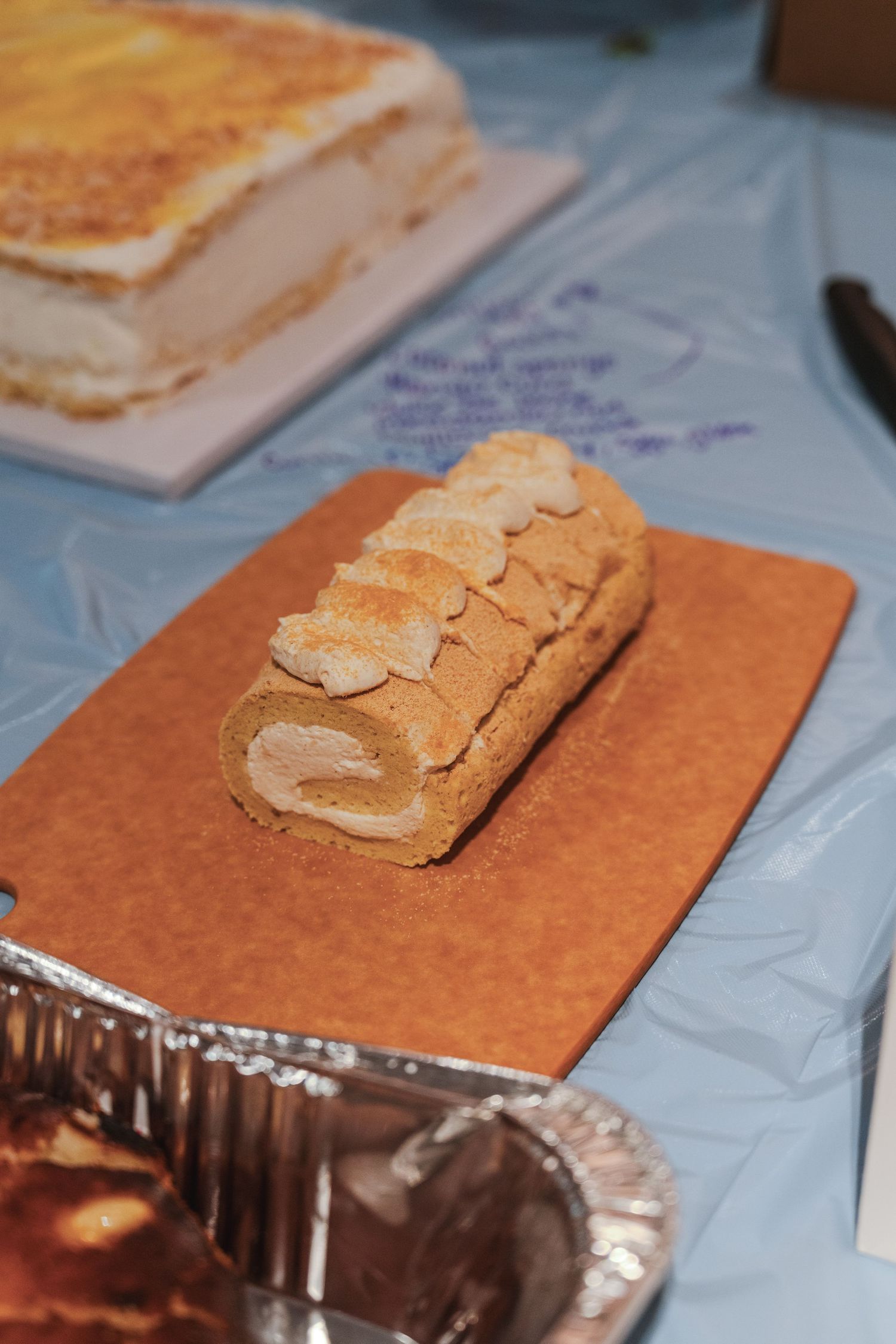 A rolled sponge cake dessert with almond slices on top sits on a brown serving board.