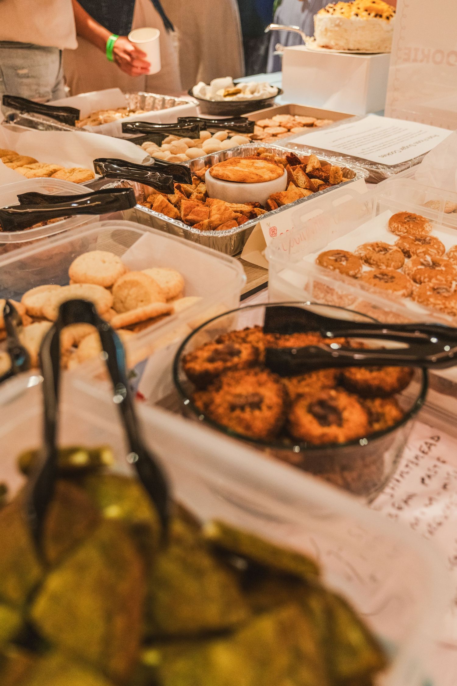 A buffet spread of cookies, pastries and appetizers laid out on white tablecloths with serving tongs and plates.
