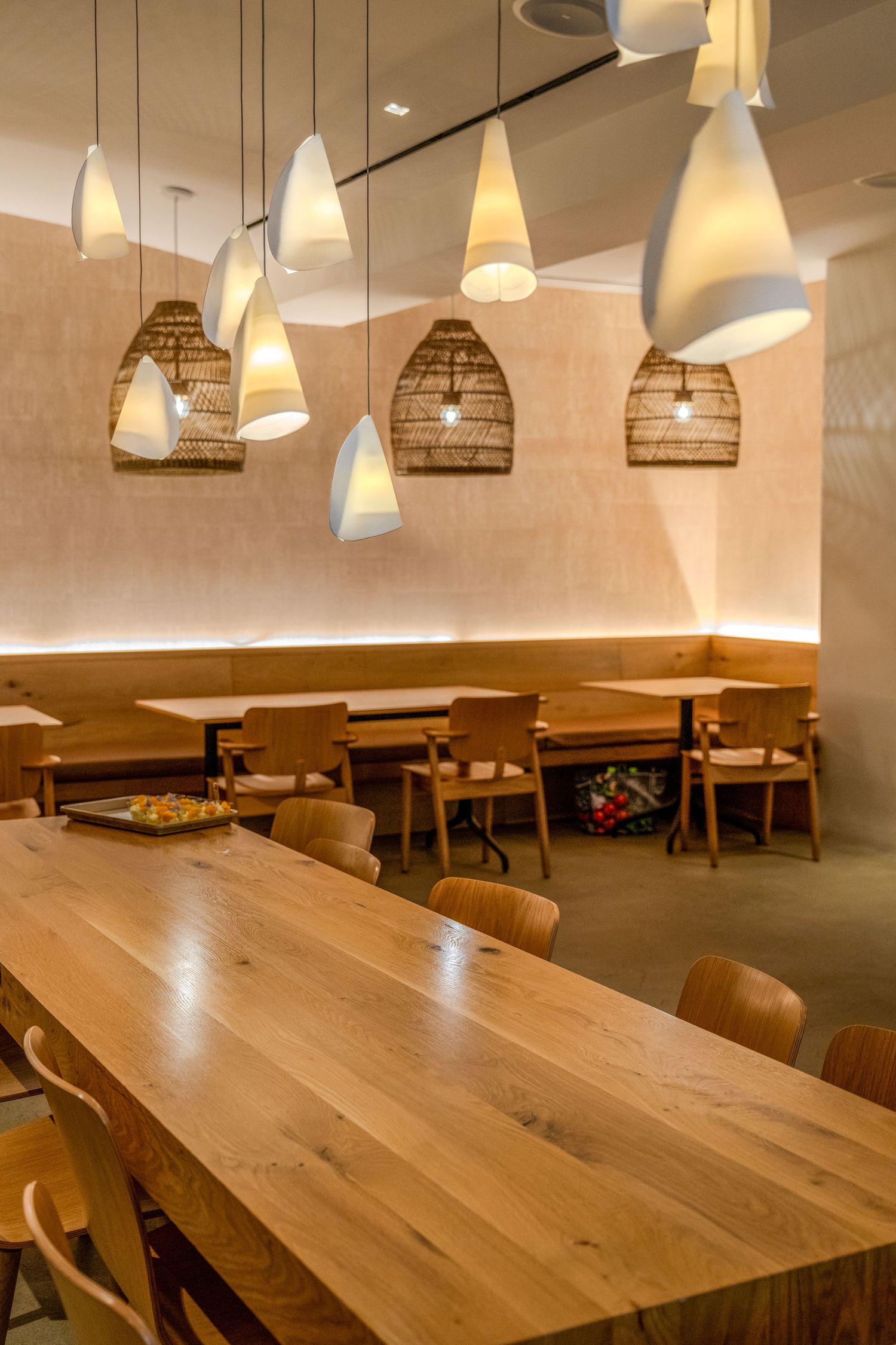 Modern restaurant interior with wooden tables and chairs illuminated by stylish pendant lights and decorative wicker lampshades.