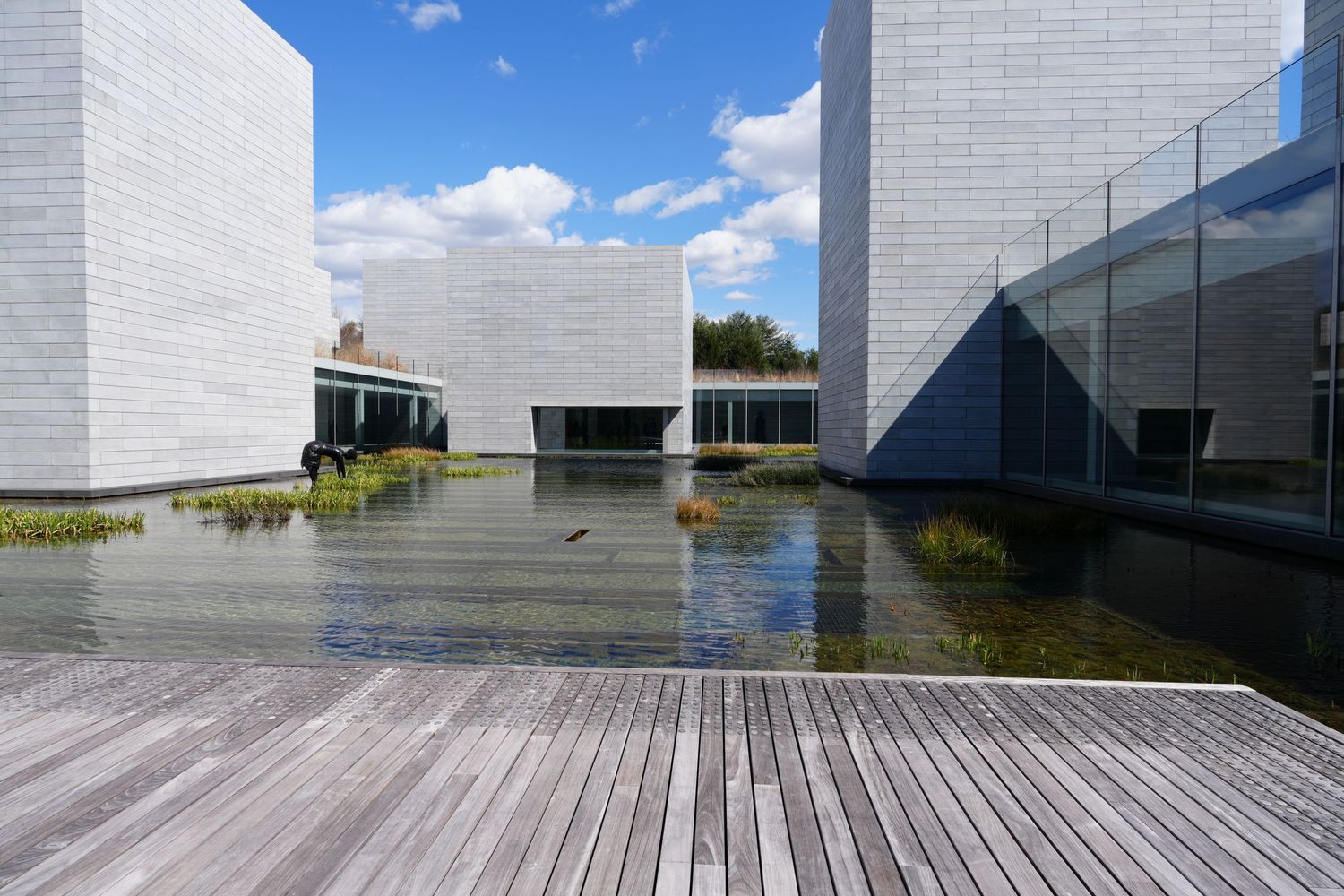 Modern architectural building with reflecting pool and wooden deck surrounded by white geometric walls.
