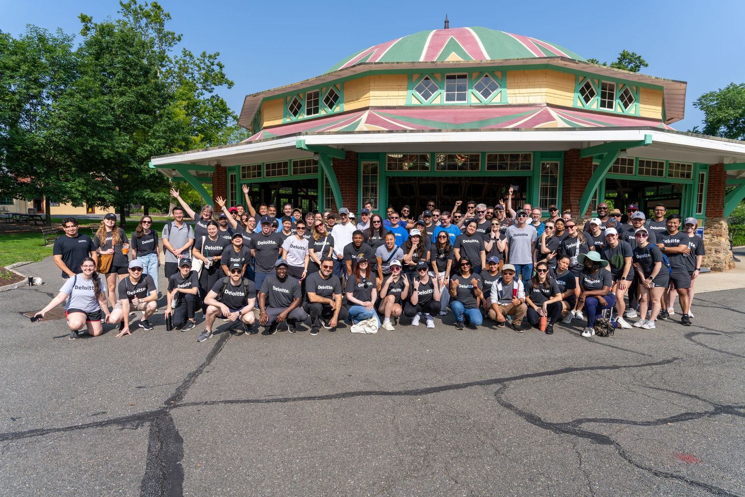 A large group gathers outside a colorful round building with a domed roof in a parking lot on a sunny day.