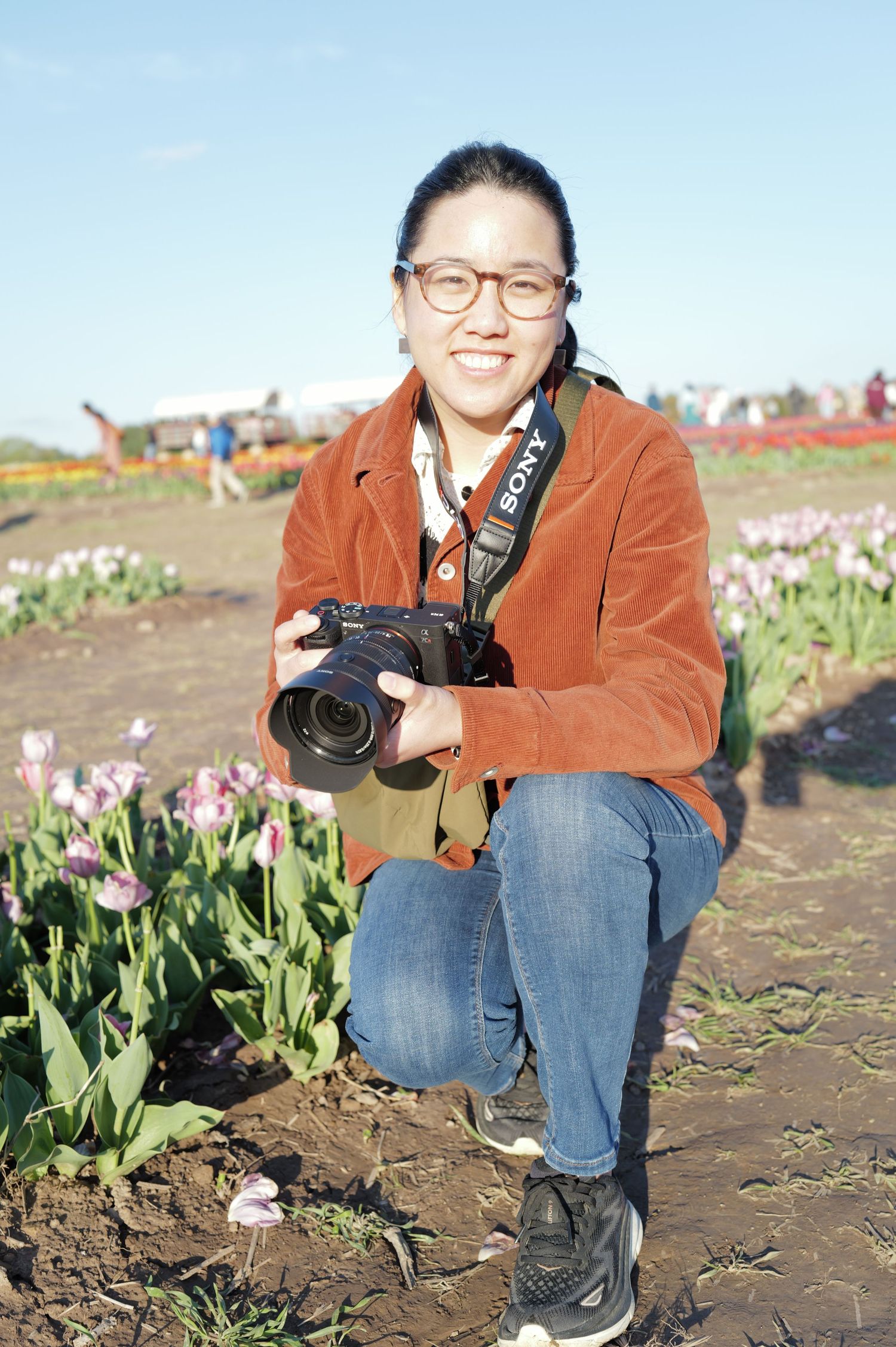 Person with camera kneeling in tulip field during springtime photography session.
