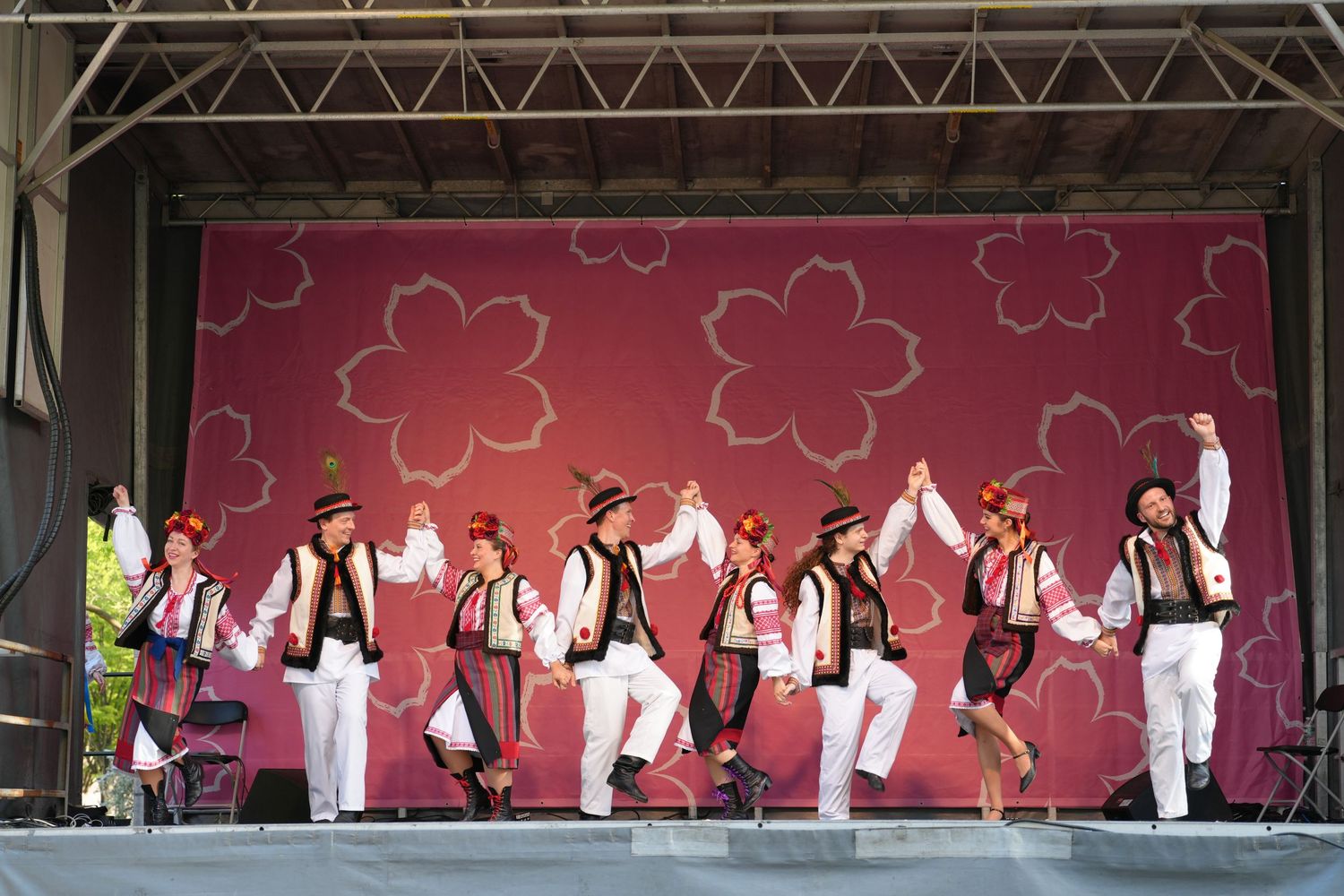 Group performance with dancers in white and black attire on stage with cherry blossom backdrop.