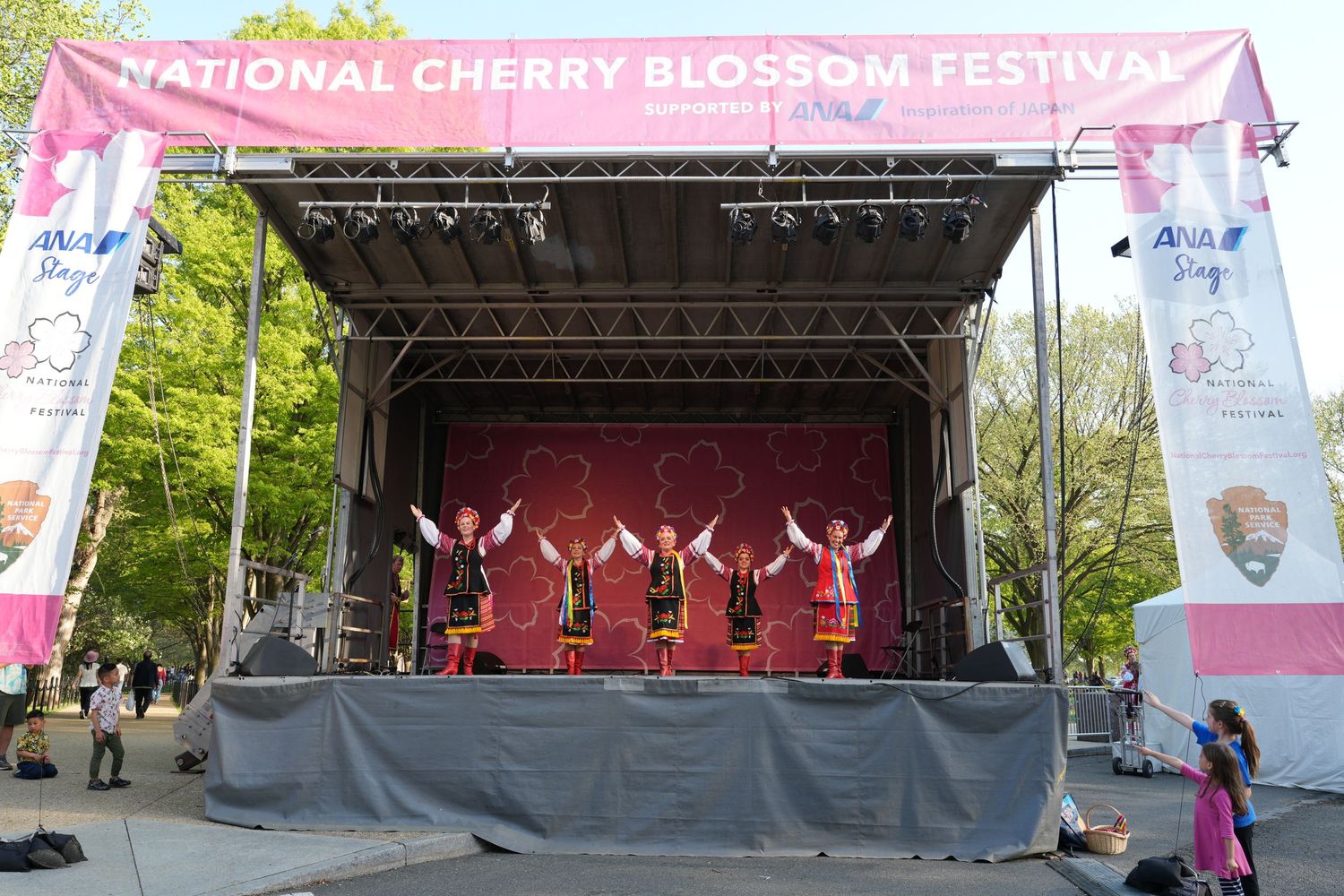 Cherry Blossom Festival stage with performers under a pink banner.