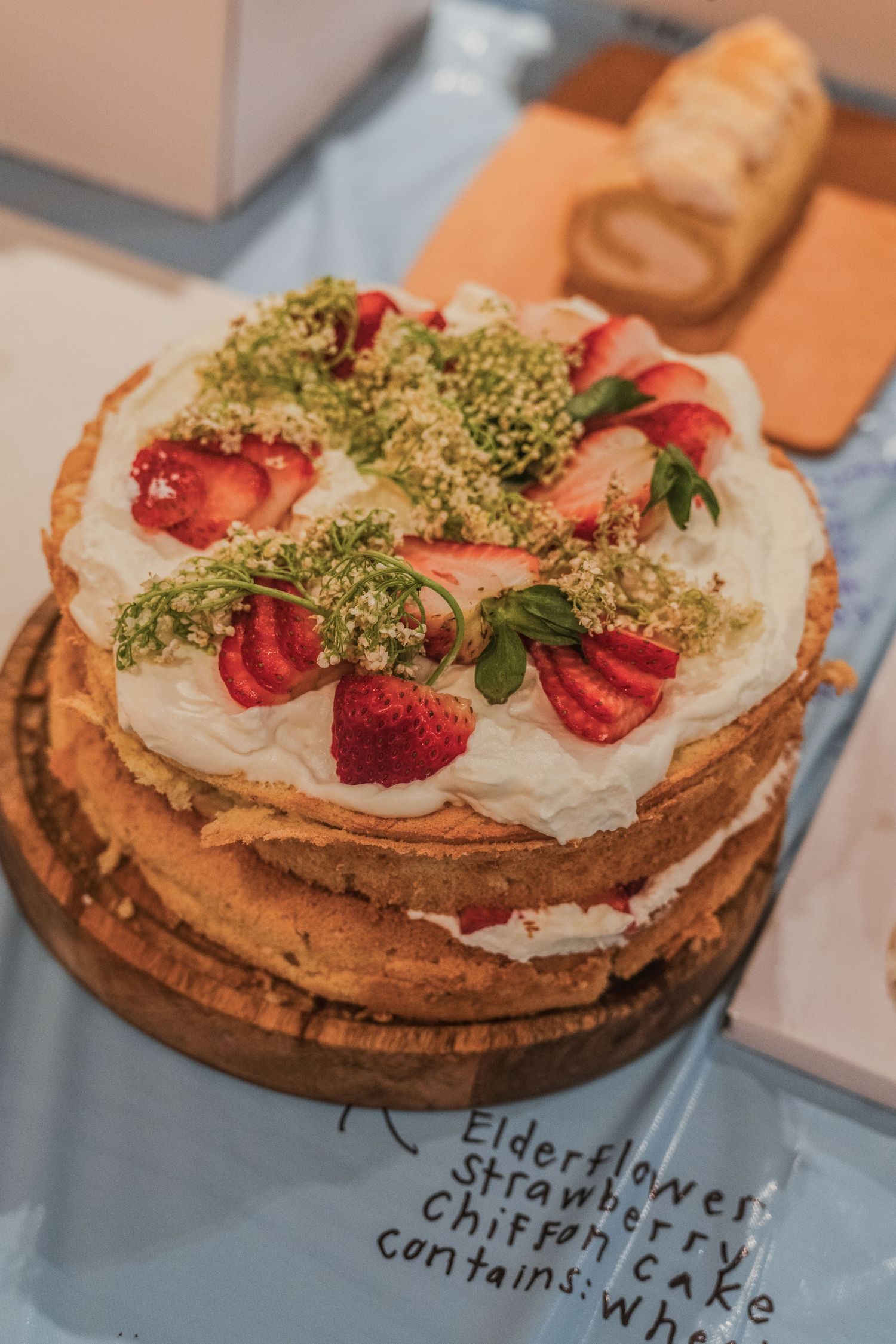 Layered cake with whipped cream, fresh strawberries and pistachio crumbs on a wooden serving board.