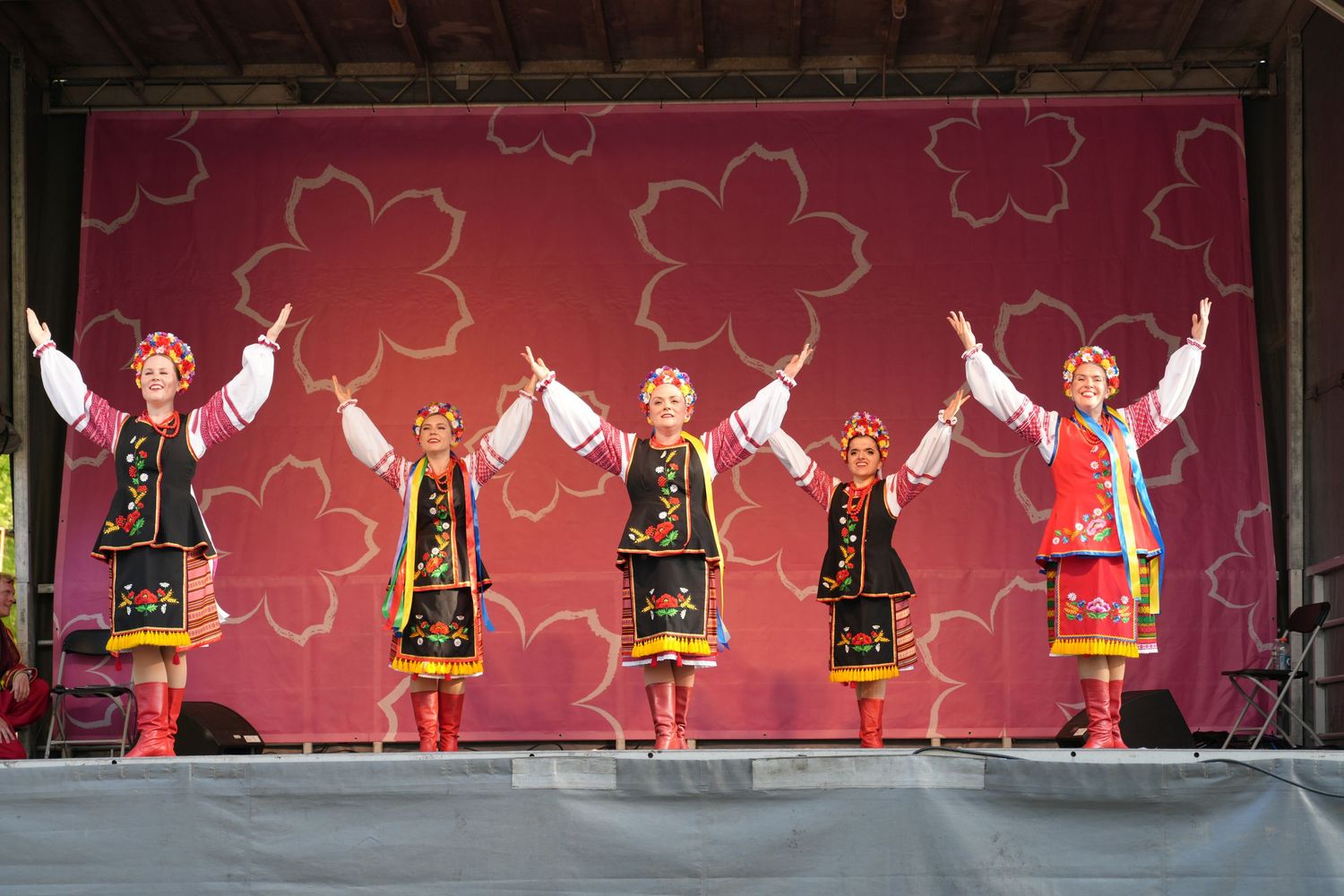 Traditional dancers in folk costumes performing on stage with cherry blossom themed backdrop.