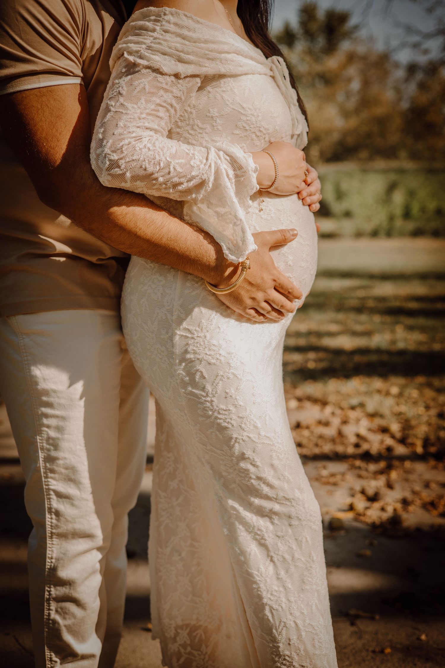 Close-up shots of a pregnant woman in white lace dress with partner's hands lovingly embracing her baby bump outdoors.