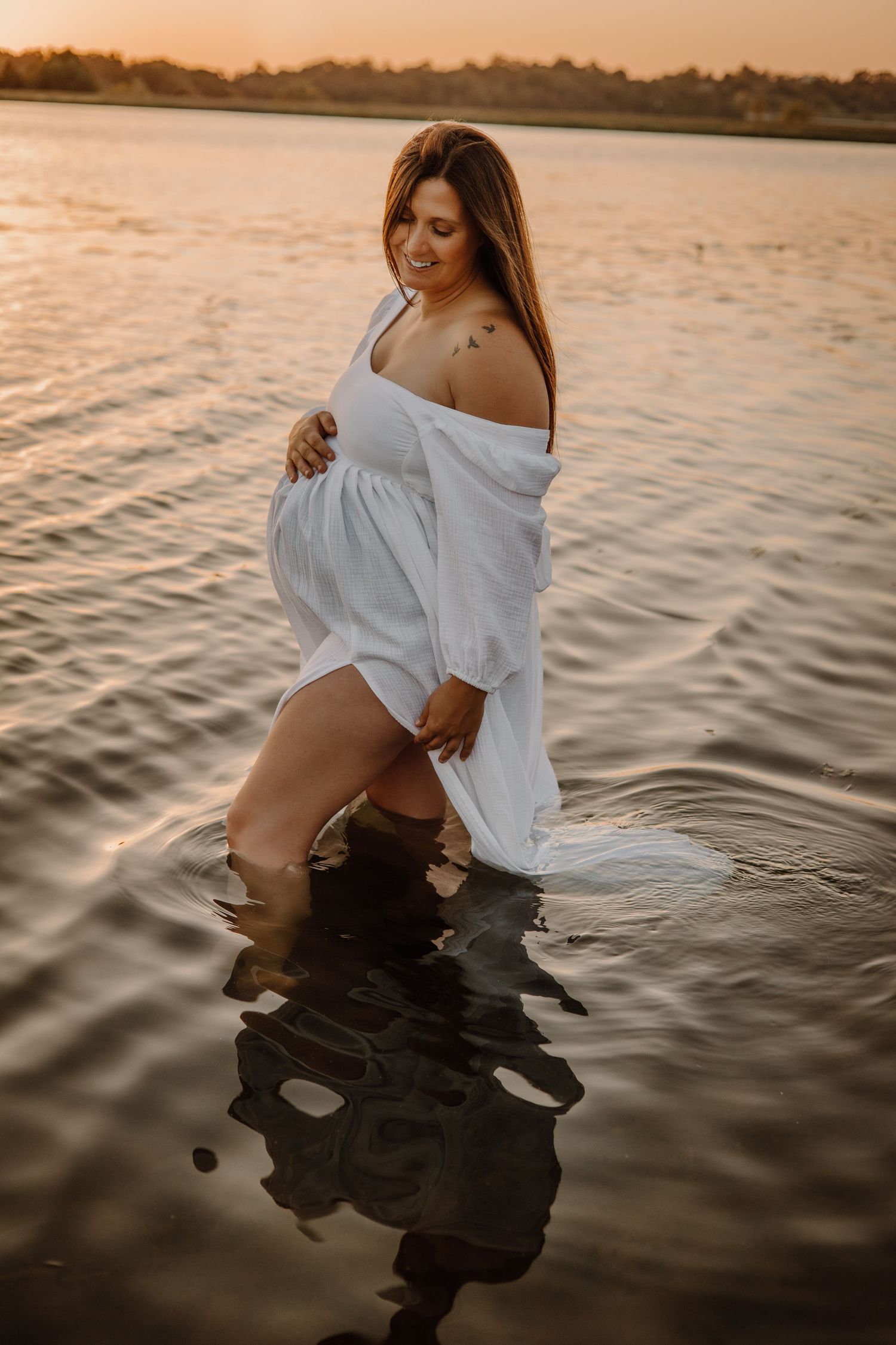 A figure in a white shirt poses in rippling water at sunset creating a dreamy reflection effect.