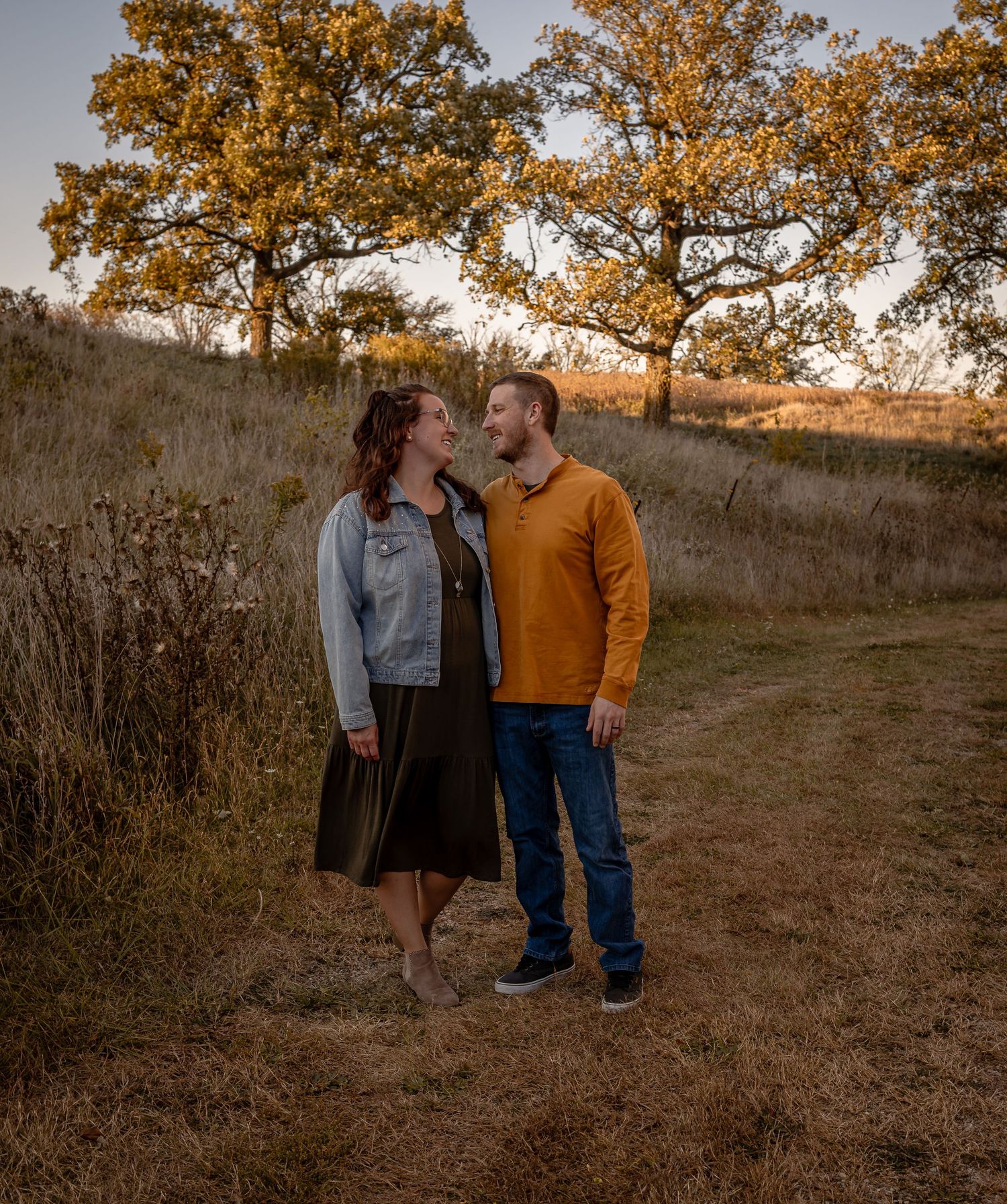Couple sharing a romantic moment at sunset on a hillside with golden autumn trees in the background.