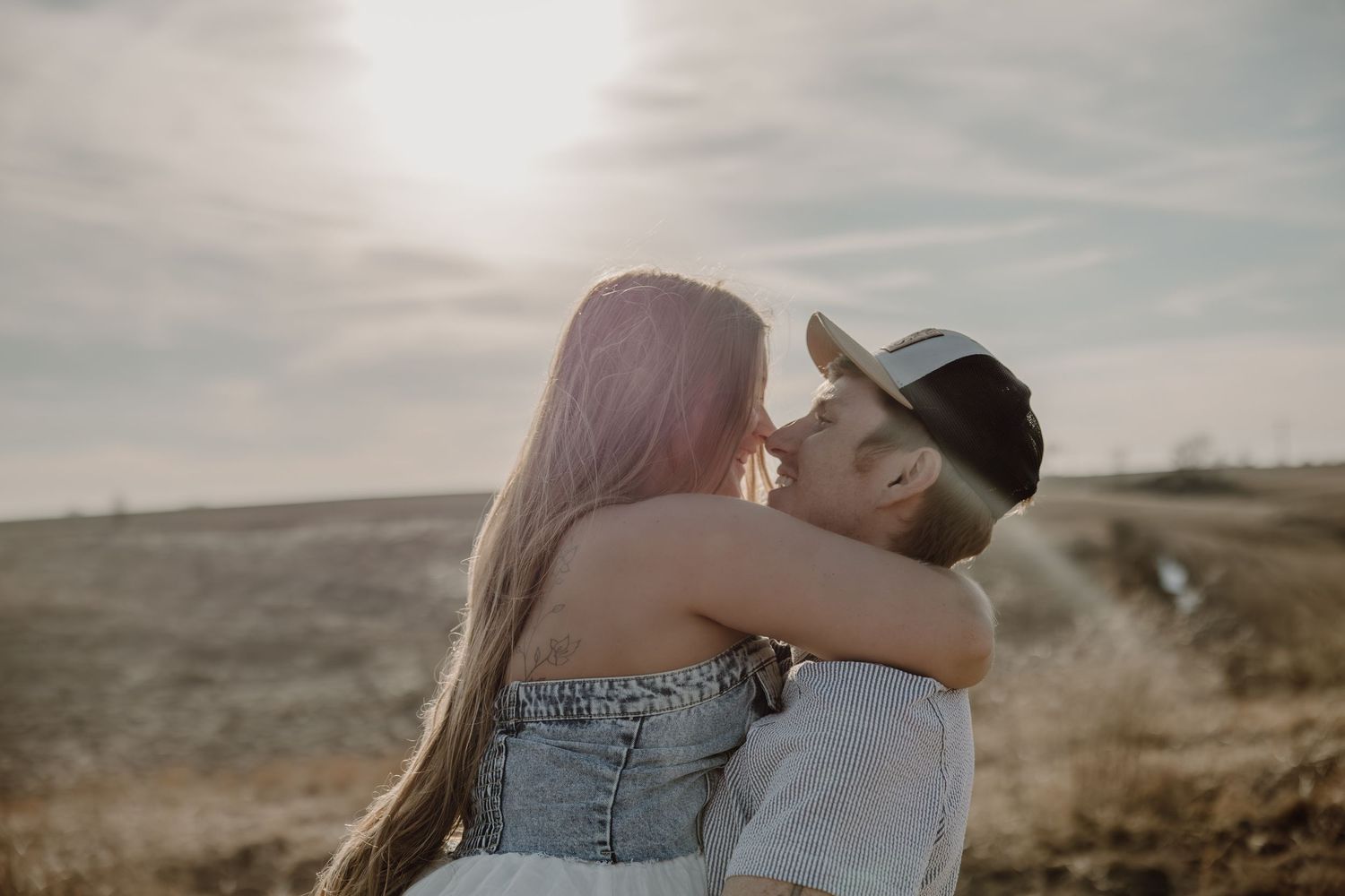 A romantic couple embraces at sunset in a desert landscape with warm golden light filtering through the clouds.