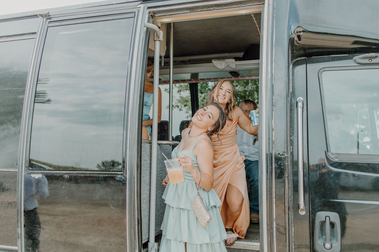 Two women laughing and posing in the doorway of a vintage silver Airstream trailer at an outdoor event.