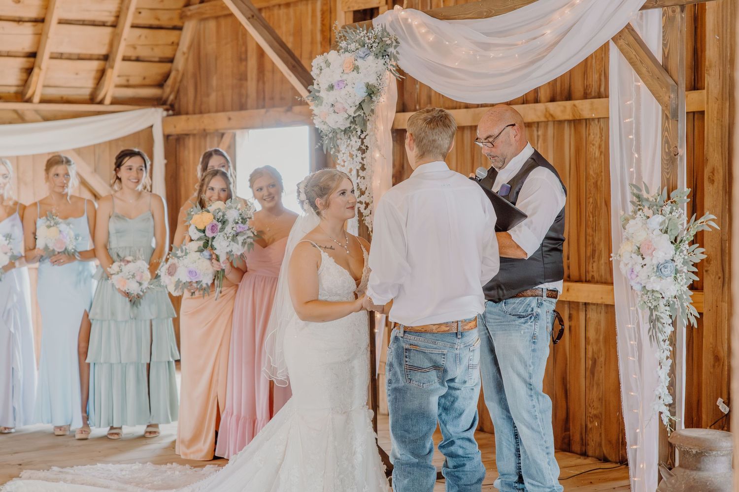 Bride and groom exchange vows at rustic barn wedding altar with bridesmaids in mint and pink gowns.