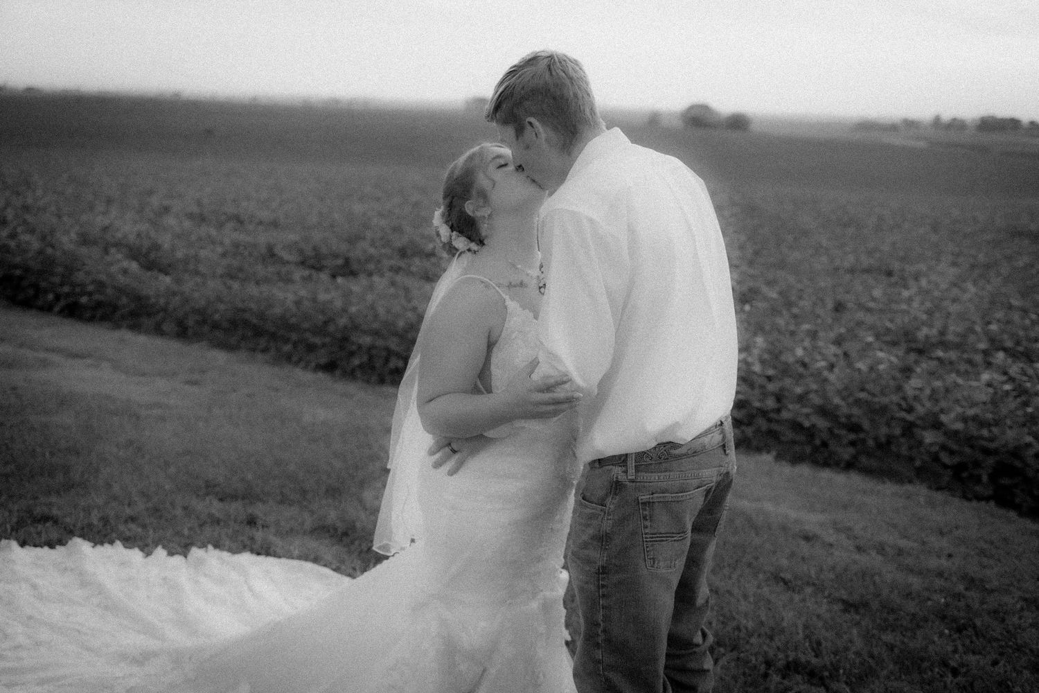 Black and white photo of a bride and groom sharing a romantic moment in a lush field on their wedding day.
