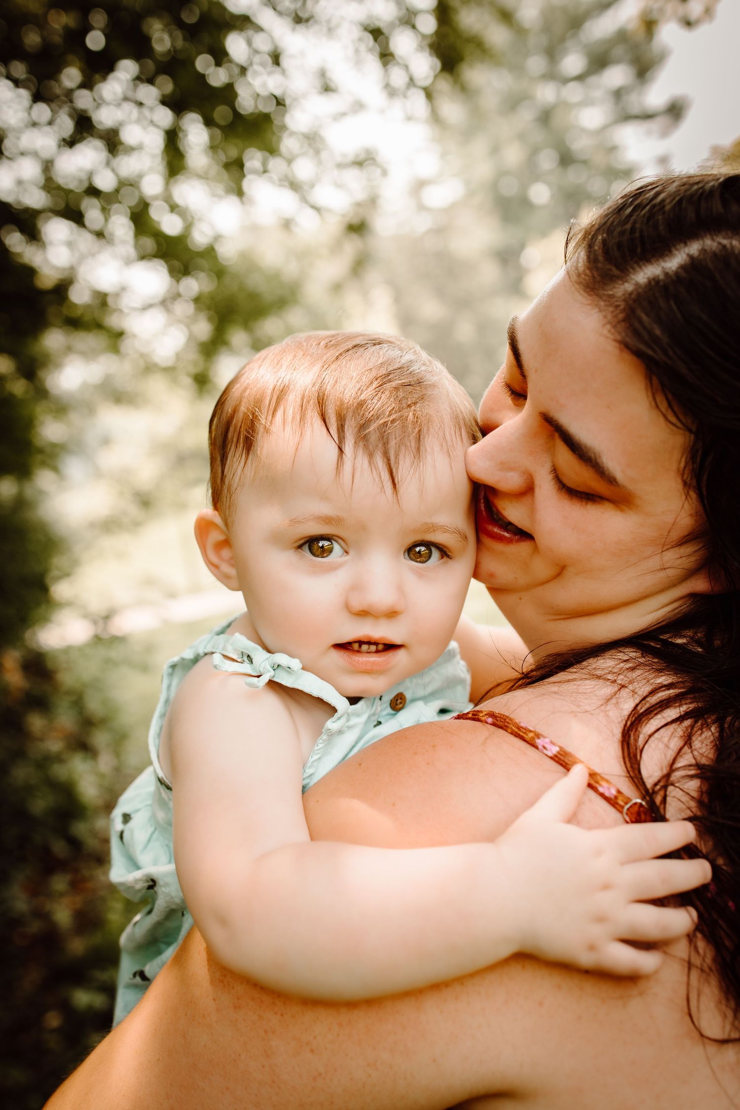 A tender moment between parent and child captured in warm sunlight during an outdoor photoshoot.