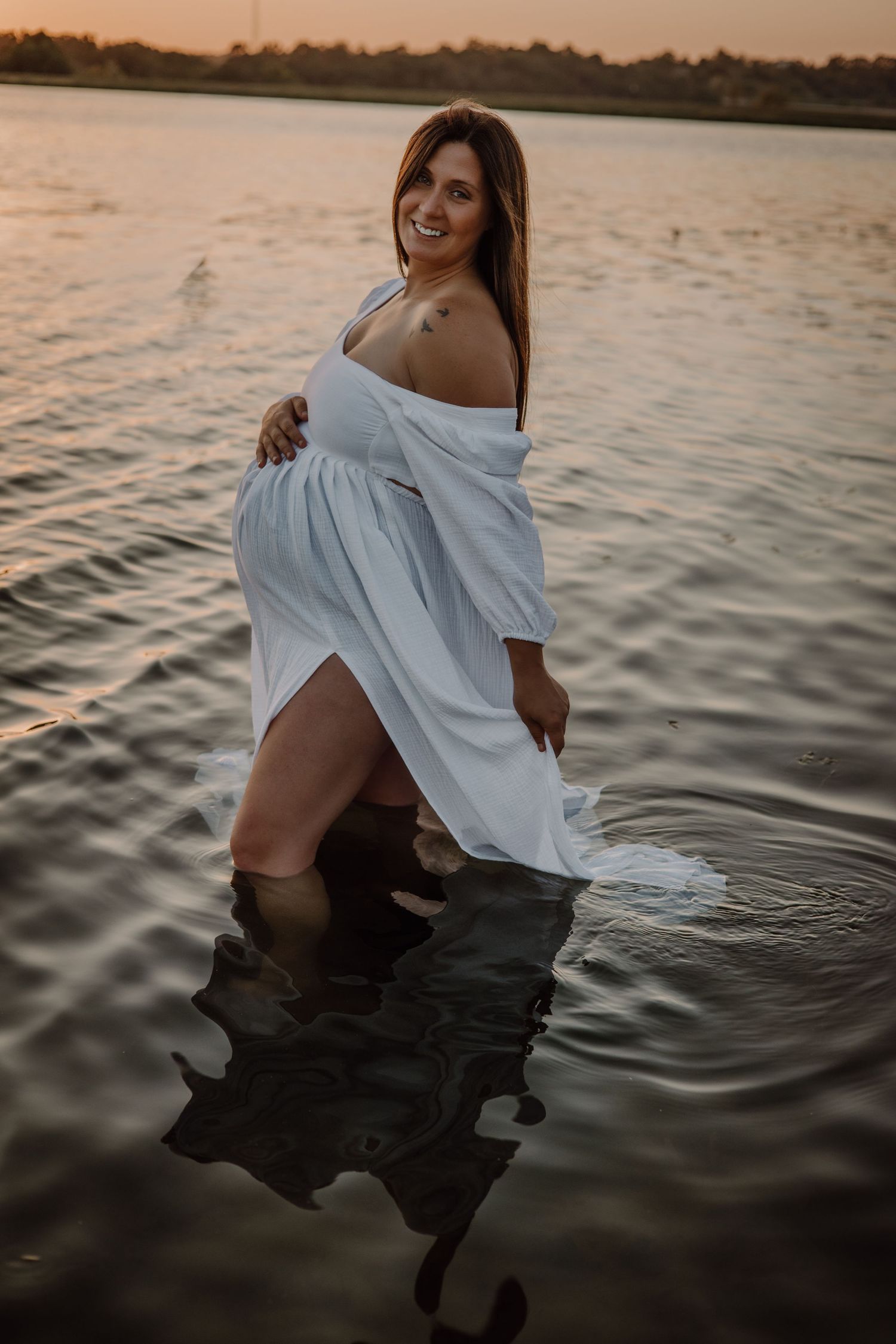 A person wearing a white dress poses in water during sunset creating a serene and artistic photoshoot series.