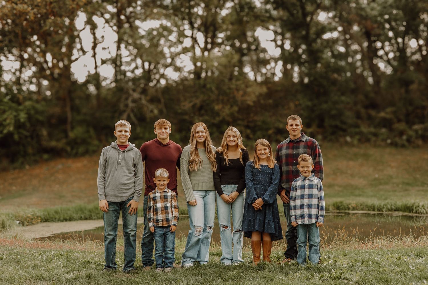 A group stands together outdoors on a grassy hill during autumn with trees in the background at sunset.