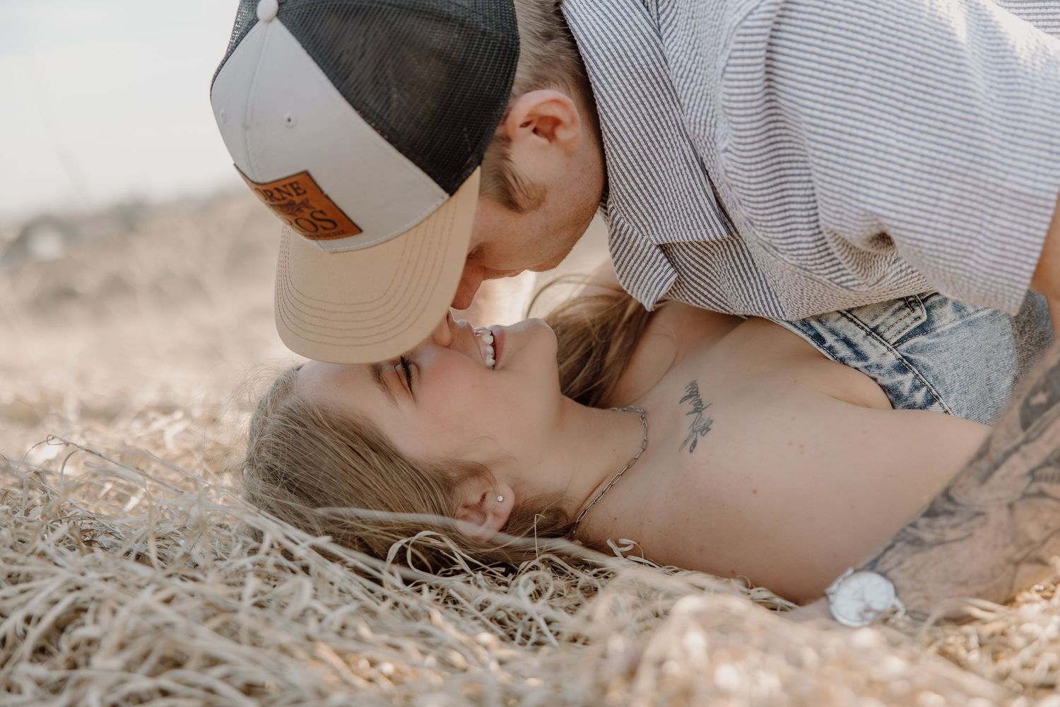 A couple in white outfits sits close together on a sandy beach at sunset, creating a romantic coastal scene.