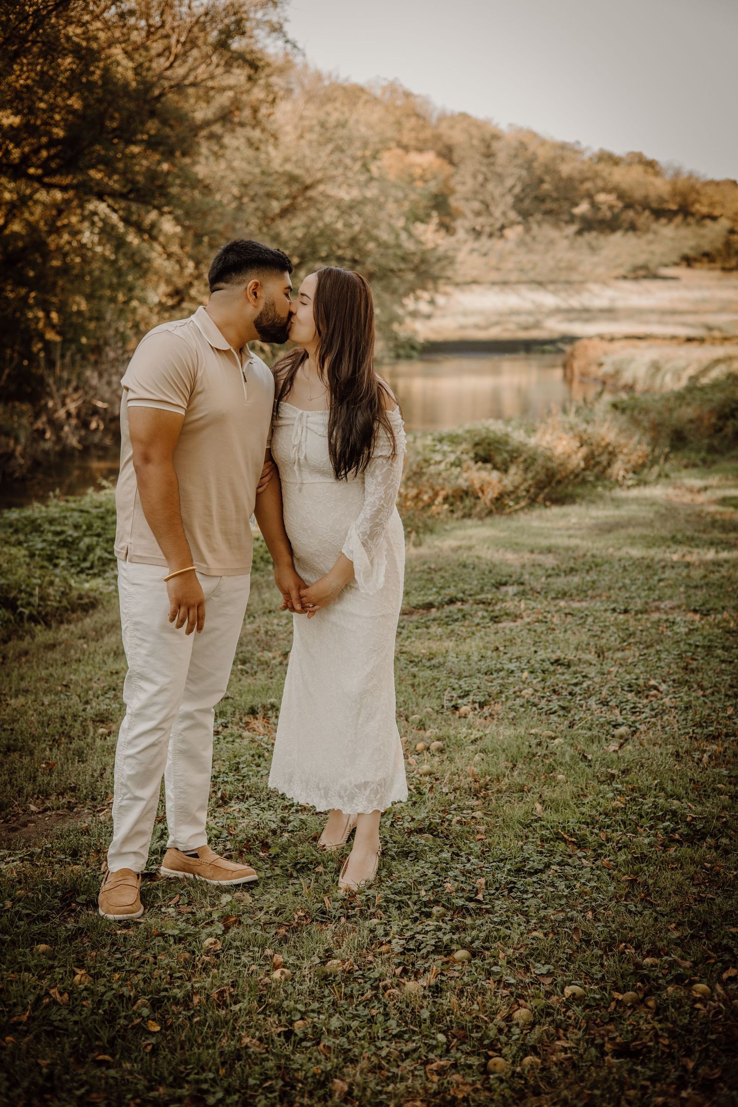 A romantic couple in white outfits walking together in a sunlit outdoor setting during golden hour.
