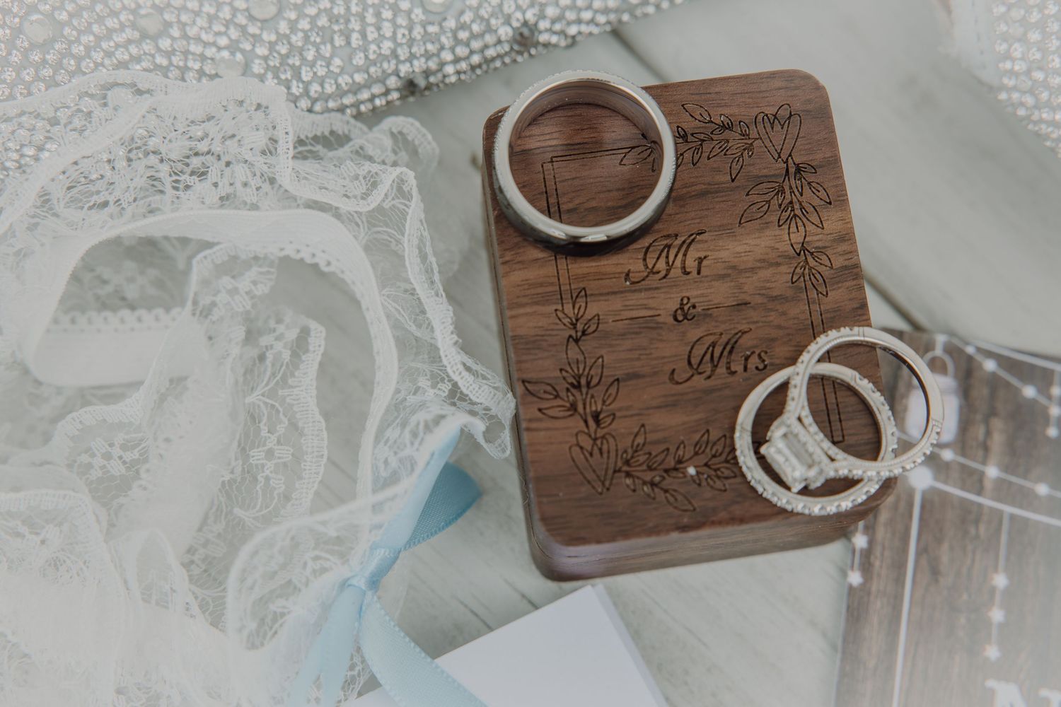 Wooden wedding ring box engraved with Mr. and Mrs. surrounded by elegant rings and white lace bridal accessories.