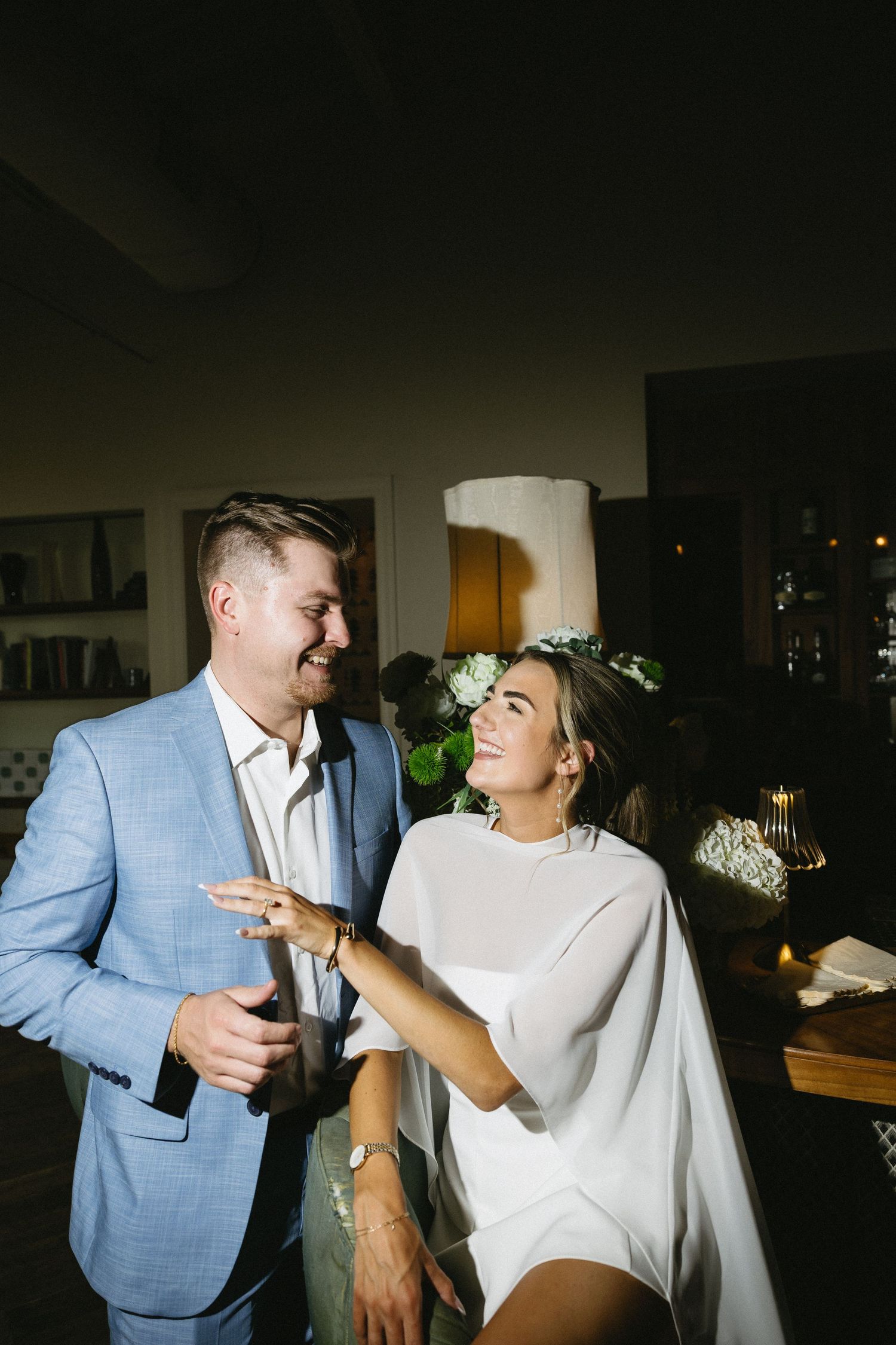 A couple in formal attire dances together playfully in a dimly lit room setting.