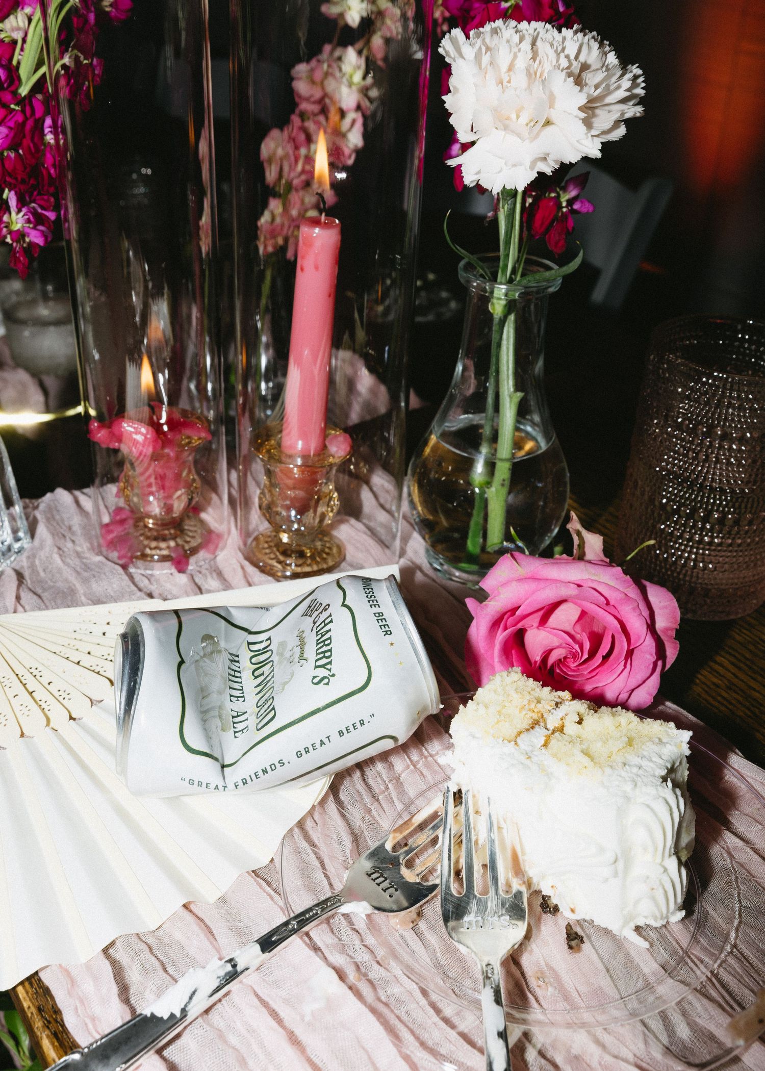 Pink and white floral table decorations with candles and scattered petals create an elegant wedding reception setting.