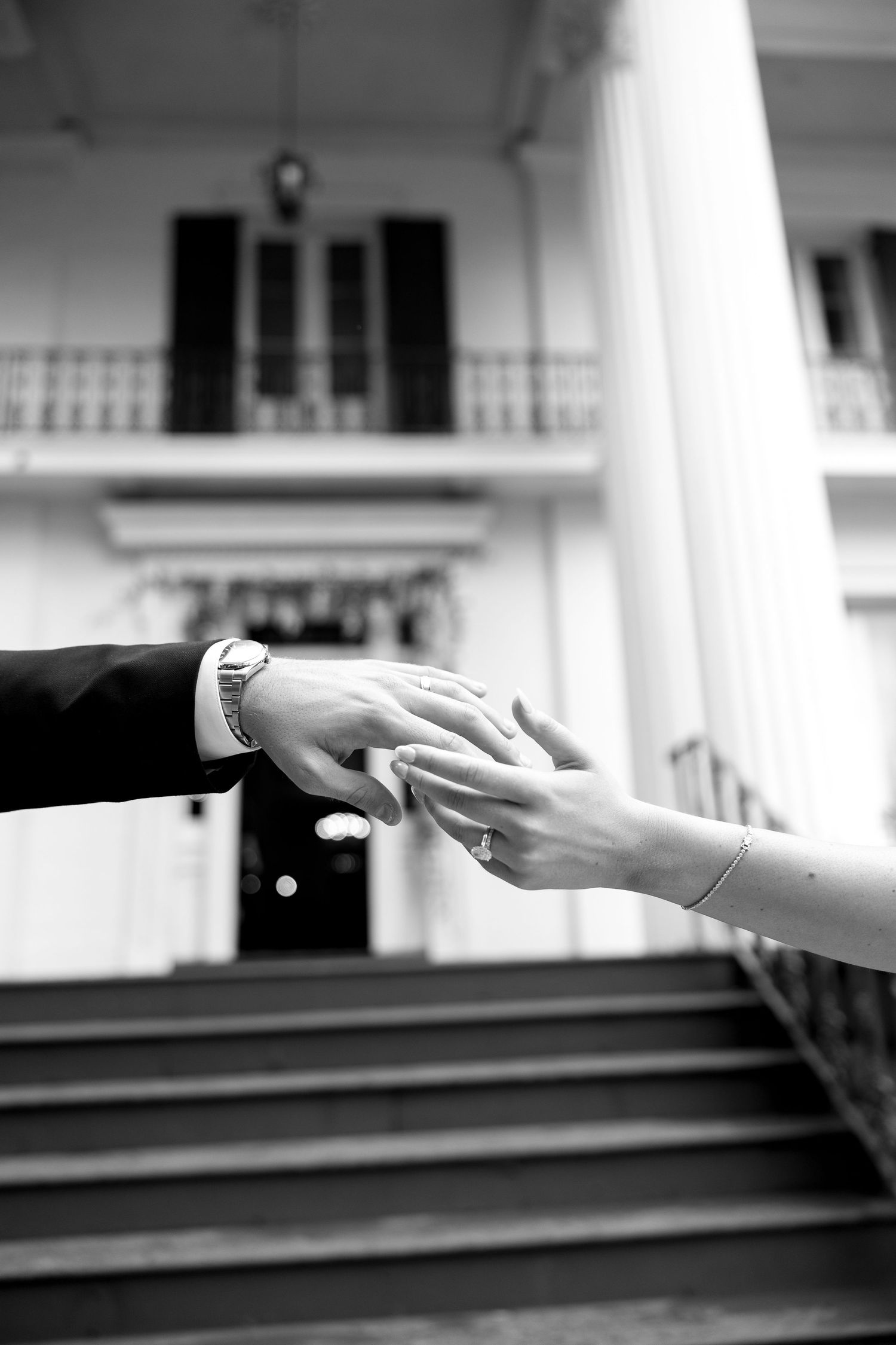 Black and white photo of couple holding hands on wedding day with elegant building columns in background.