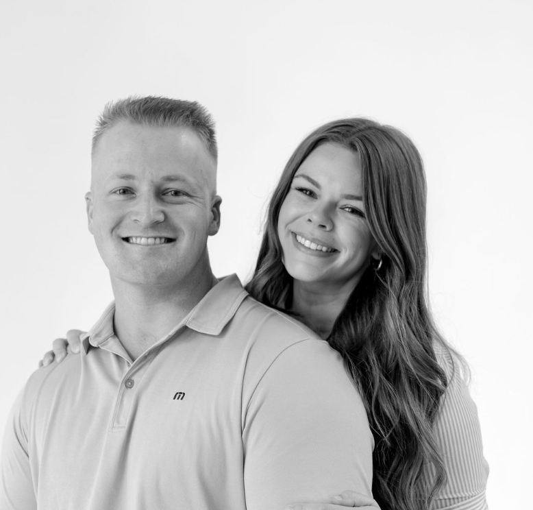 Black and white portrait of a smiling couple posing together against a white background.