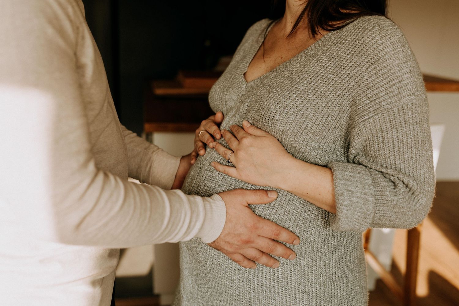 Séance photo grossesse à domicile, futurs parents posant les mains sur le ventre de la future maman dans une atmosphère intime
