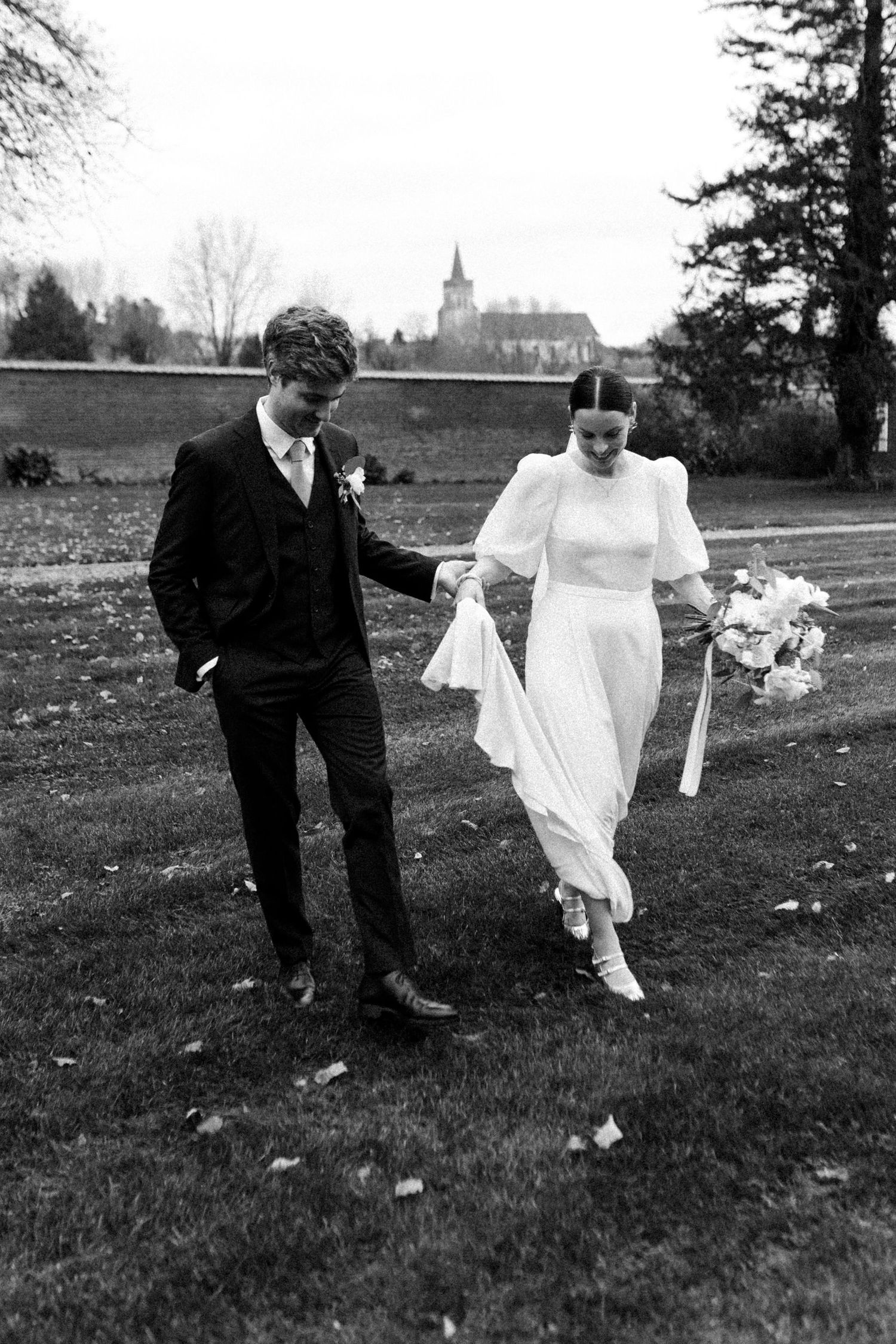Couple de mariés marchant main dans la main, photographie de mariage en reportage noir et blanc.