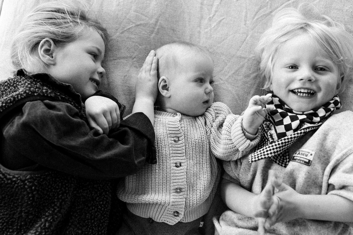 Fratrie allongée côte à côte lors d’une séance photo famille lifestyle en noir et blanc à Lille