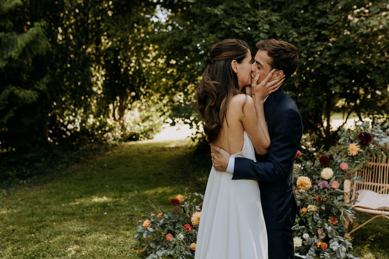 Mariés s’embrassant dans un jardin fleuri, moment intime et naturel lors de leur journée de mariage.