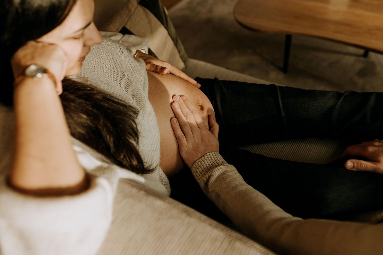 Séance photo grossesse lifestyle : mains posées sur un ventre rond, moment intime et authentique photographié à la maison.