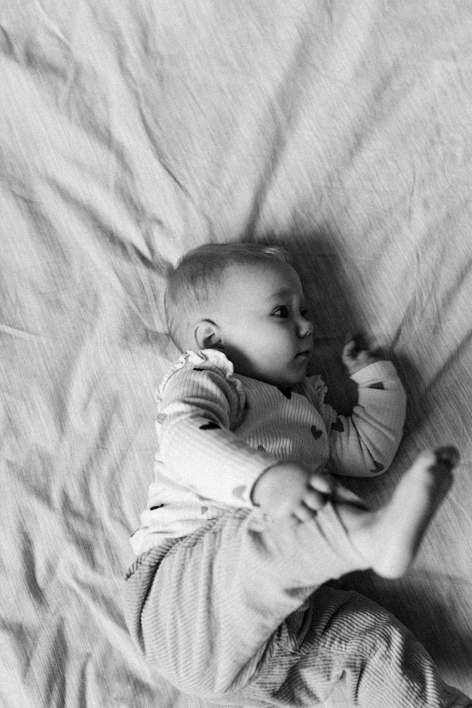 Photographie de nouveau-né en noir et blanc : détail d’un bébé allongé, image douce et intemporelle prise en lumière naturelle.