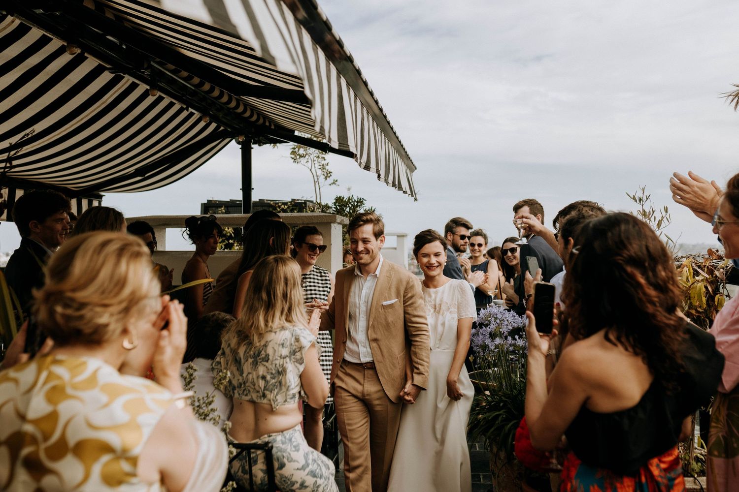Mariage en reportage naturel : les mariés sortent de la cérémonie entourés de leurs invités, sous une pluie de pétales, capturés sur le vif.