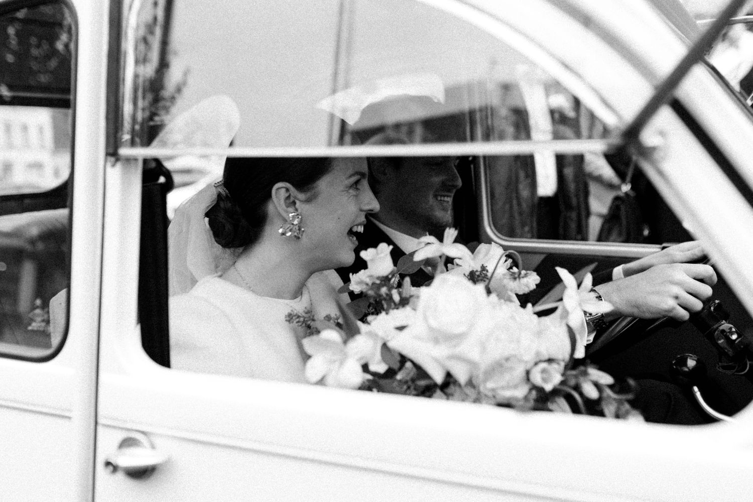 Couple de mariés souriant dans une voiture ancienne après leur cérémonie, photographie de mariage naturelle et émotionnelle Anaïs Bizet